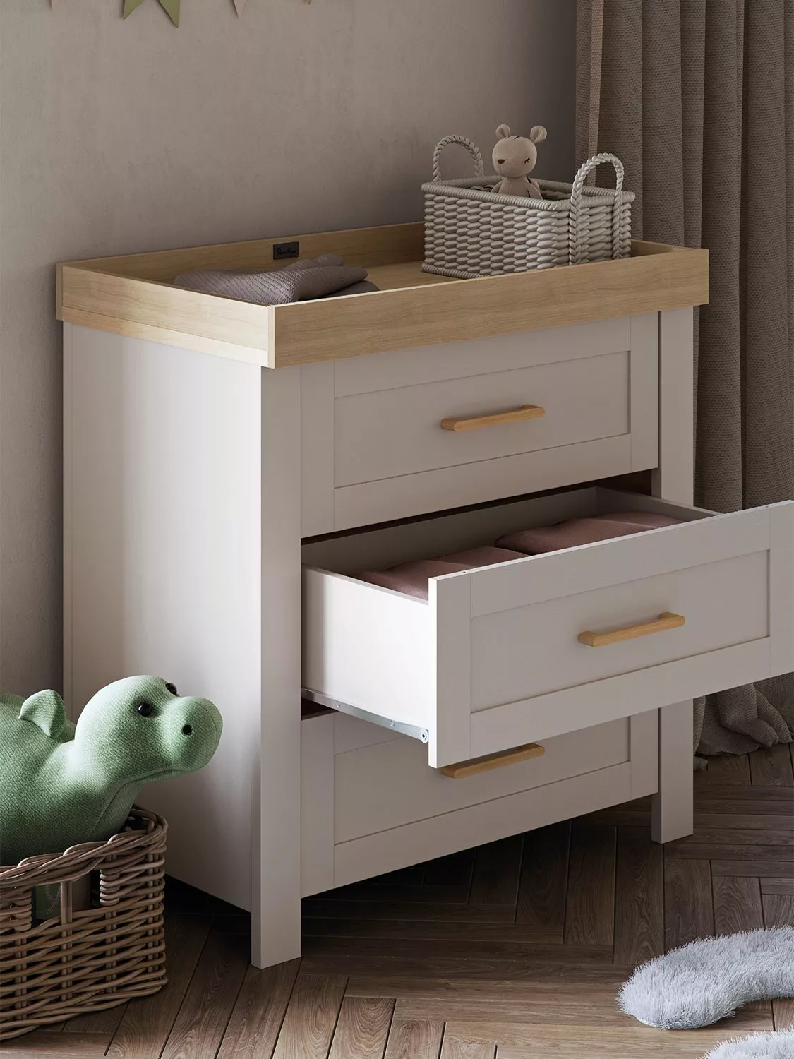 White and oak baby changing table with drawers, wicker basket and soft toys in a cosy nursery room