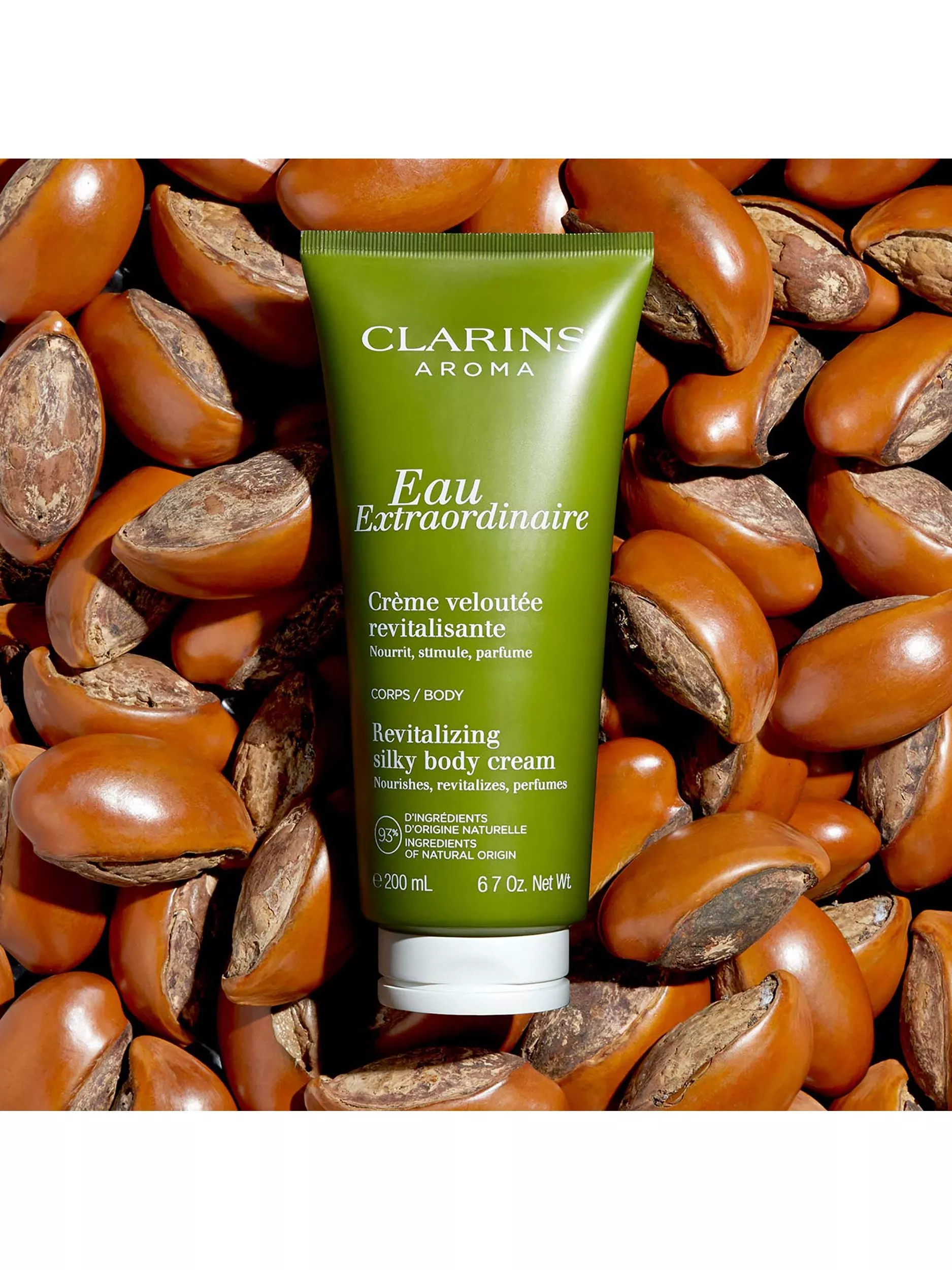 Green tube of Clarins Eau Extraordinaire body cream on a background of brown seeds, highlighting its natural origin.