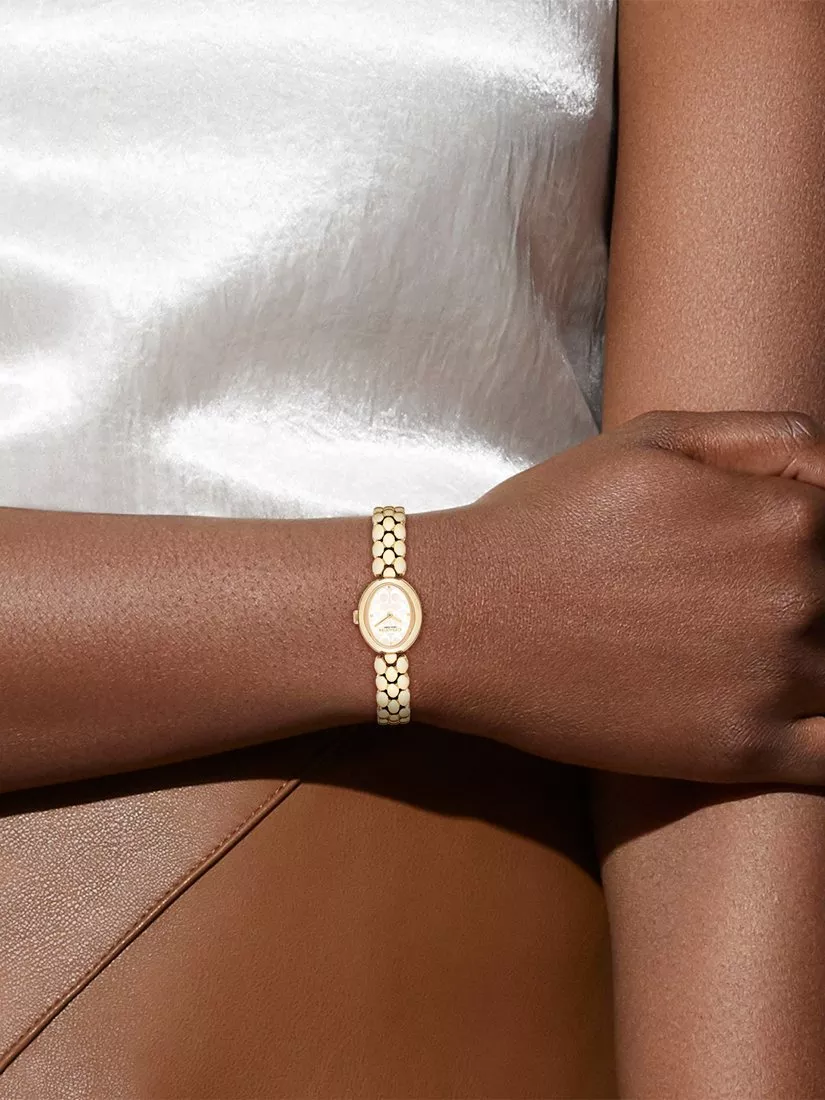 Gold chain necklace with stacked gold rings, including a rainbow gemstone band, on a light stone surface