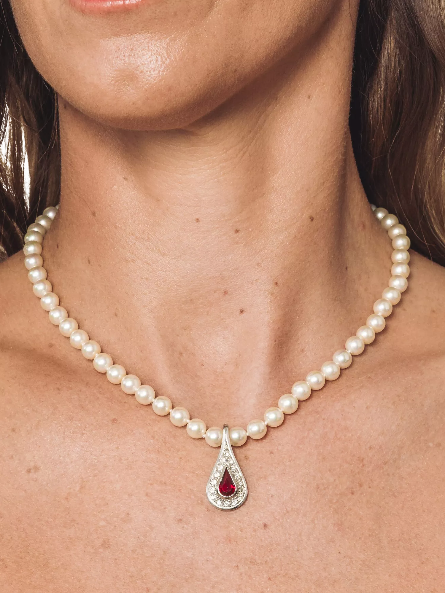 Close-up of woman wearing pearl necklace with ruby teardrop pendant and diamond setting