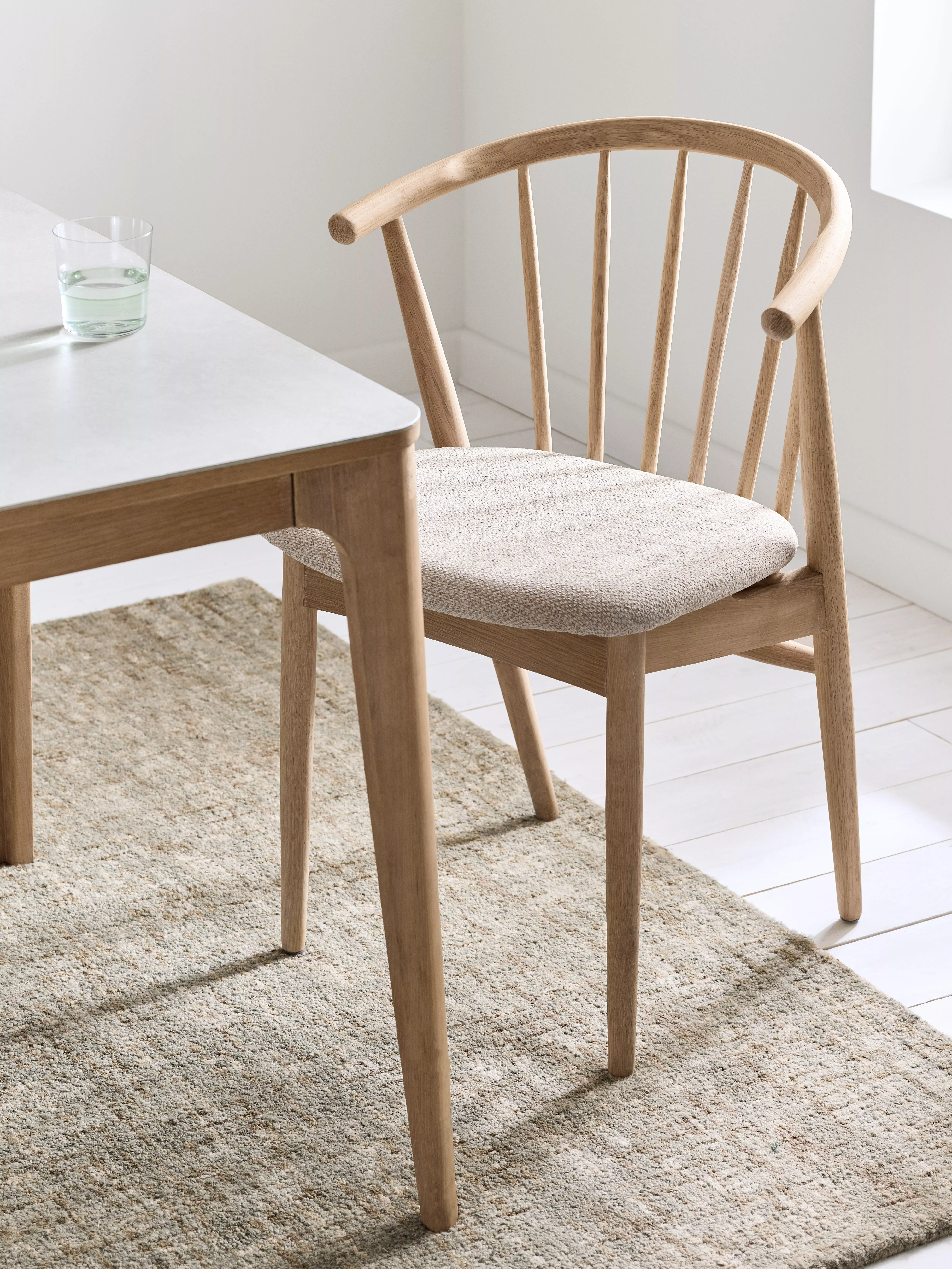 Scandinavian oak dining chair with upholstered seat beside modern table, minimalist bright dining room setting
