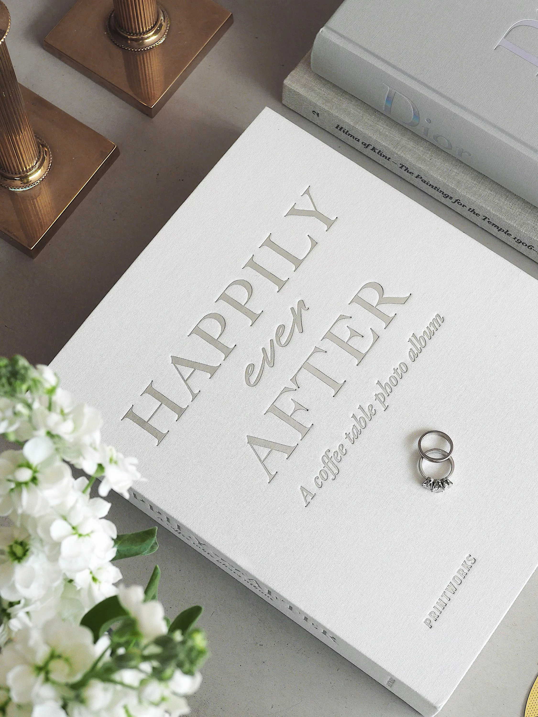 Happily Ever After coffee table photo album with wedding ring, books, brass candleholders and flowers on table