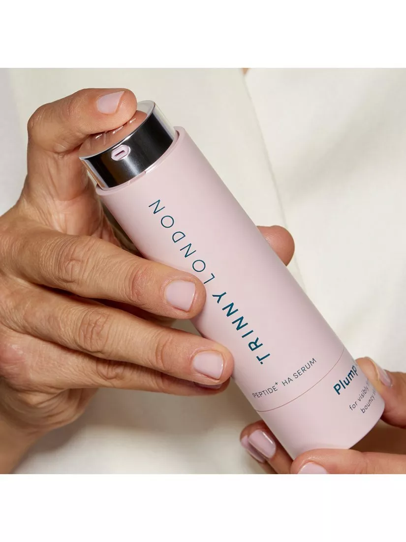Hands holding TRINNY LONDON Plump Peptide + HA serum in pink bottle, close-up skincare product shot