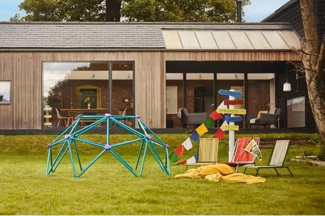 Modern house with large windows, colourful garden play area, and decorative signs on a lush green lawn.