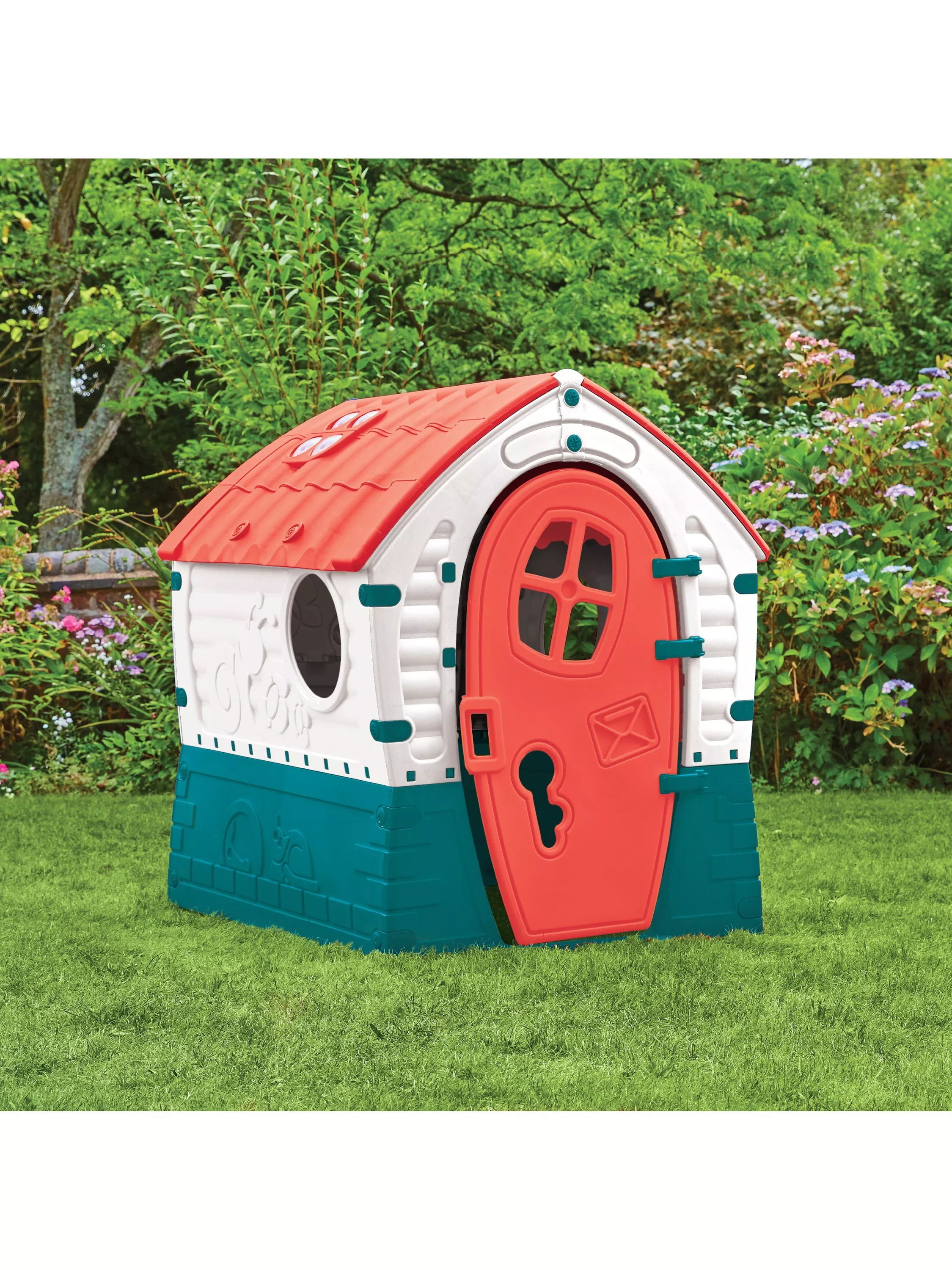 A colourful children's playhouse with a red roof and door, set in a lush garden surrounded by greenery.
