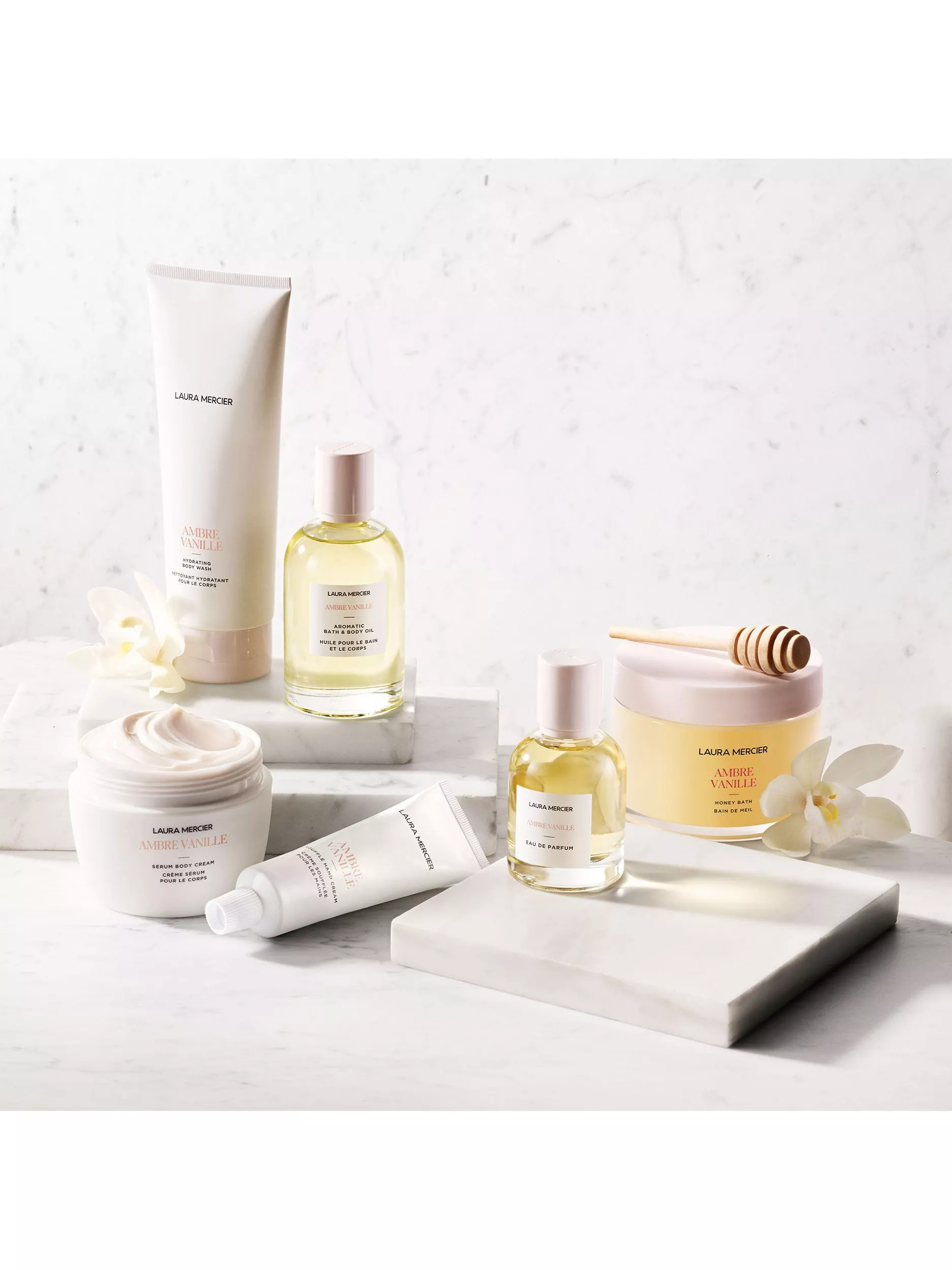 Laura Mercier Ambre Vanille body care and perfume set on marble with honey dipper and white flowers