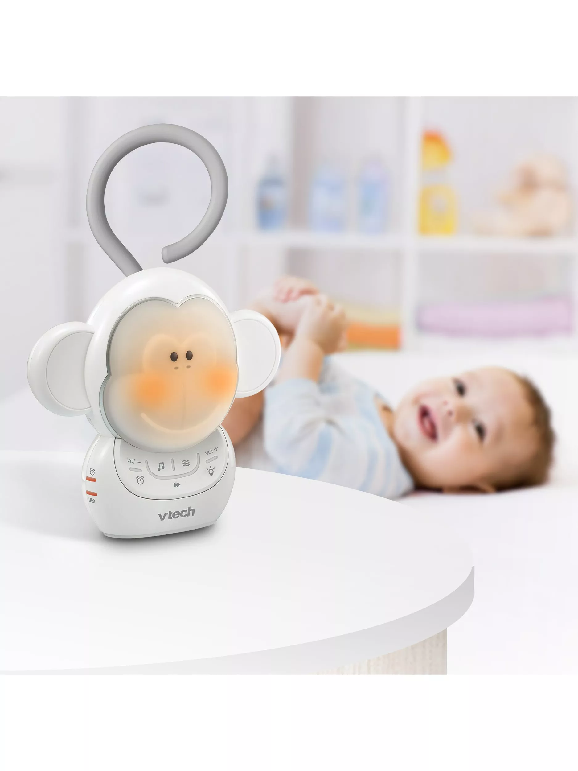 VTech baby monkey night light with music controls on table, with baby lying on bed in nursery background