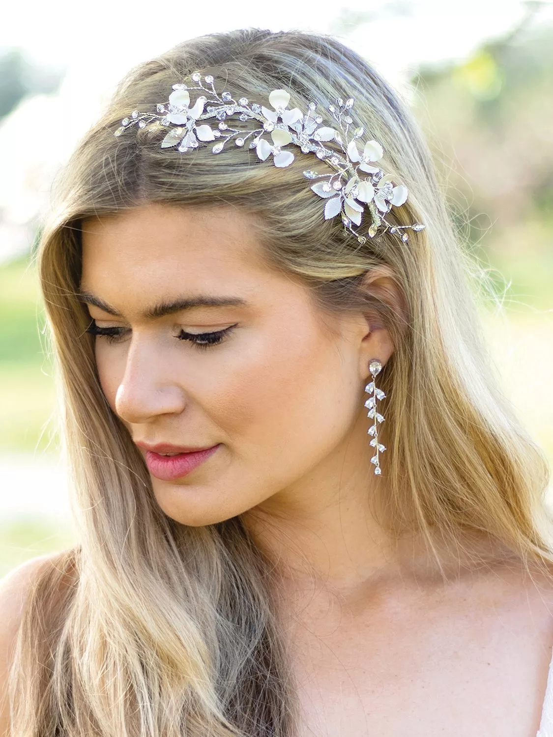 Bridal floral crystal hair vine on blonde woman with drop earrings, close-up outdoor wedding portrait.