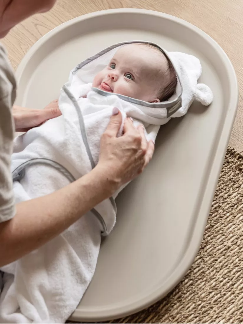 Newborn baby wrapped in a hooded towel on a changing mat after bath time, parent gently drying and cuddling