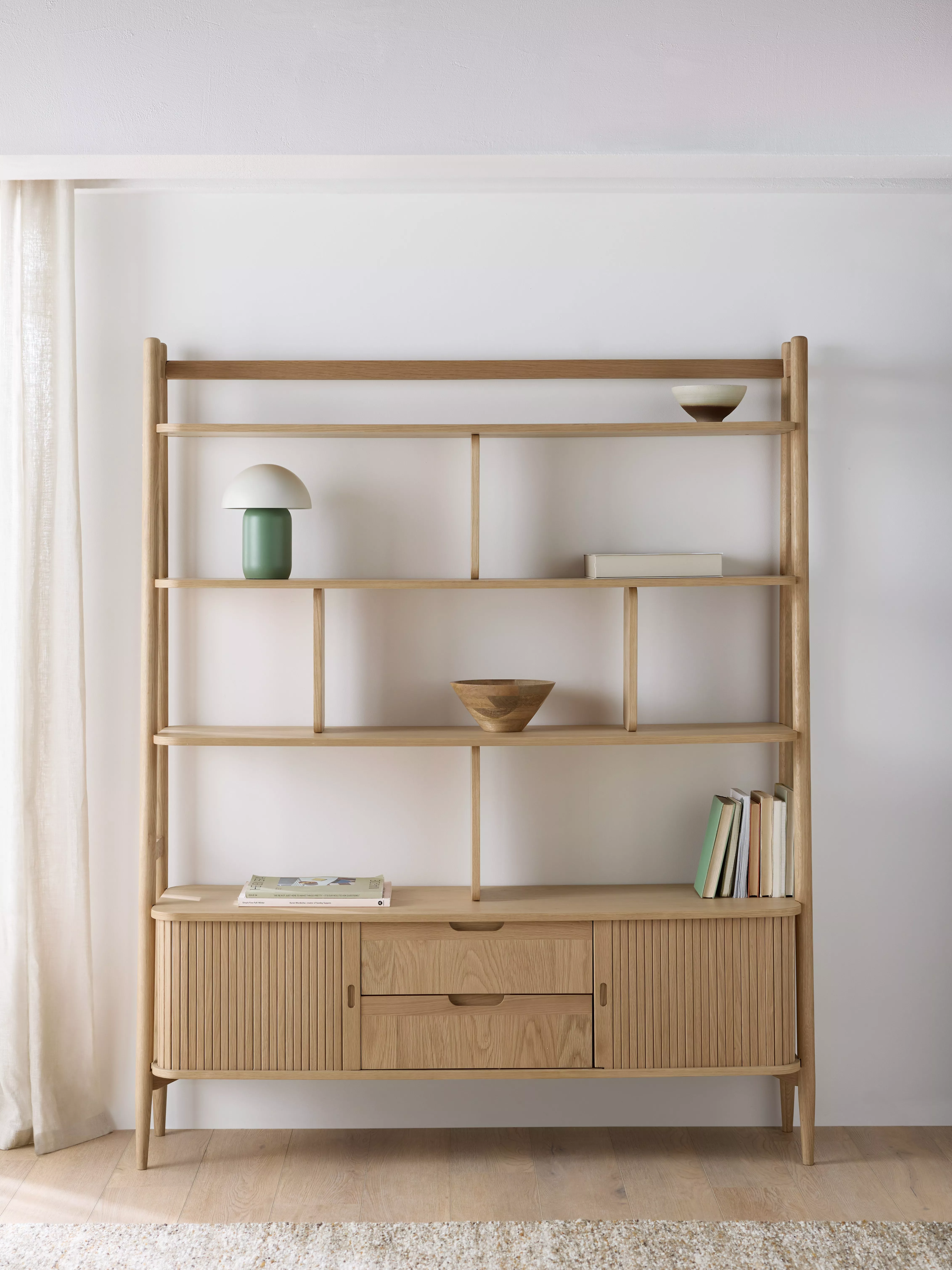 Minimalist oak shelving unit with drawers, styled with books, bowls and lamp in bright neutral room
