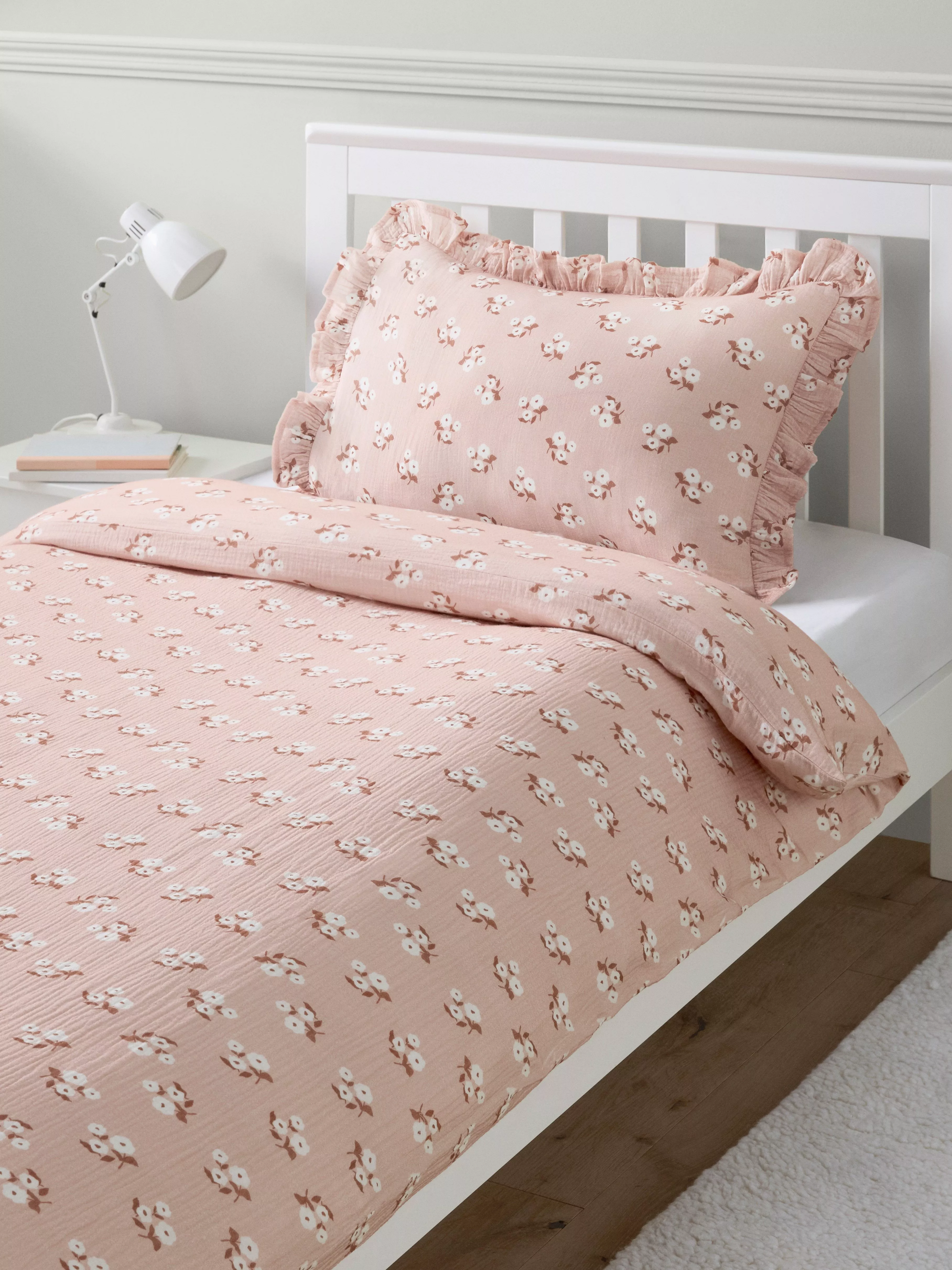Blush pink floral duvet cover set with ruffled pillowcase on white bed frame in modern bedroom setting