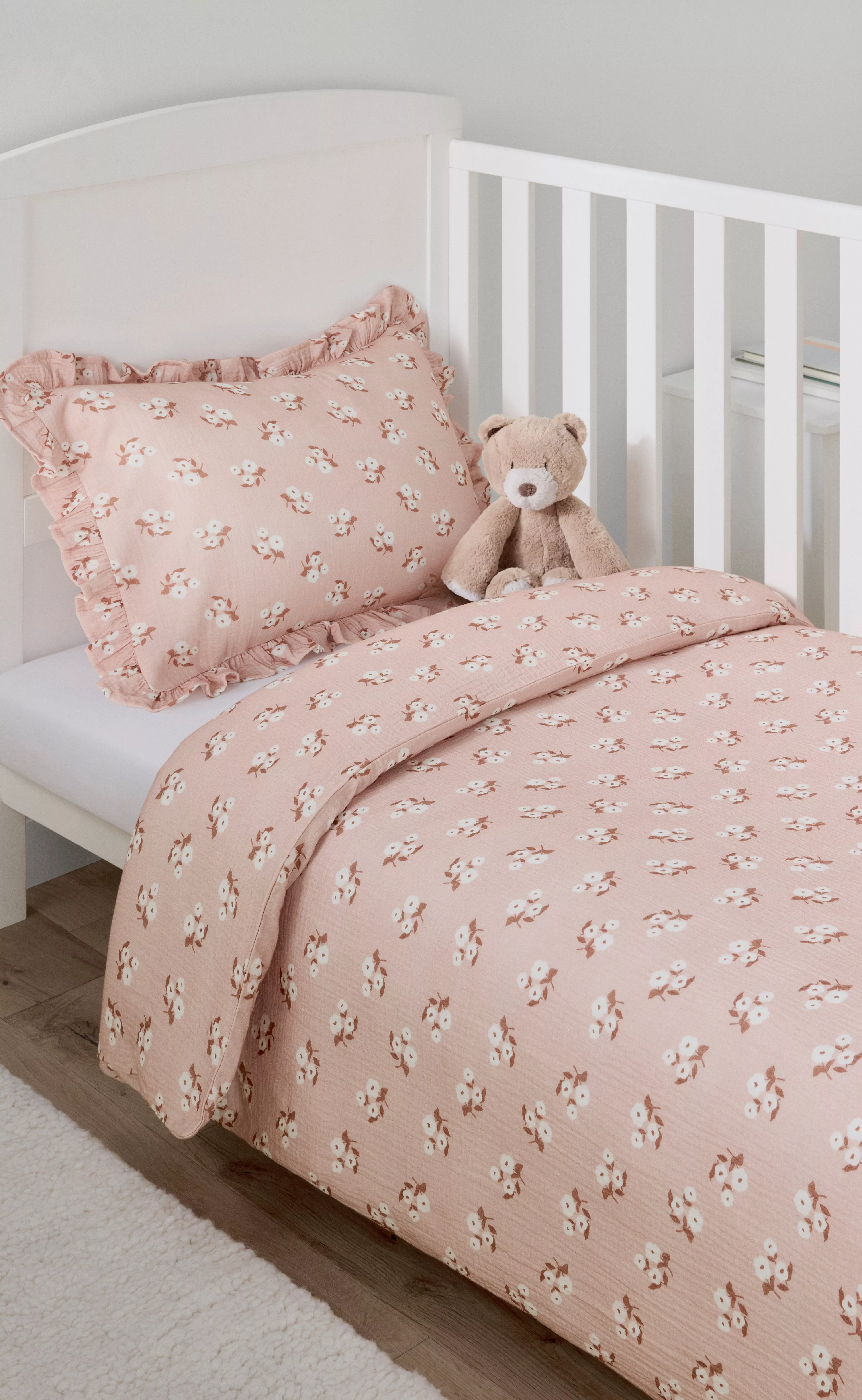 White cot with blush pink floral nursery bedding set, ruffled pillowcase and duvet, teddy bear on mattress