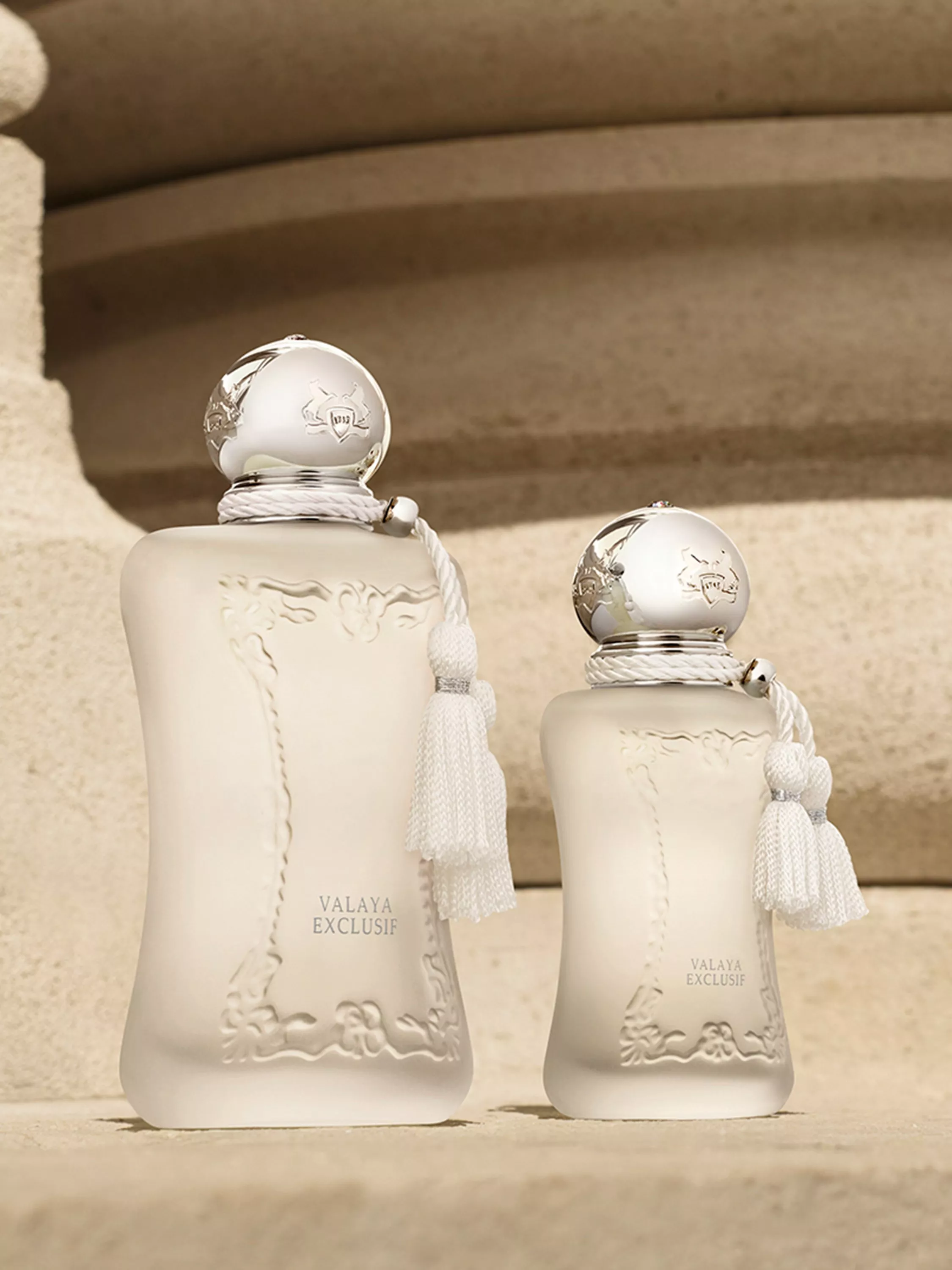 Three pink perfume bottles with silver caps and tassels on a white pedestal, luxury fragrance product shot