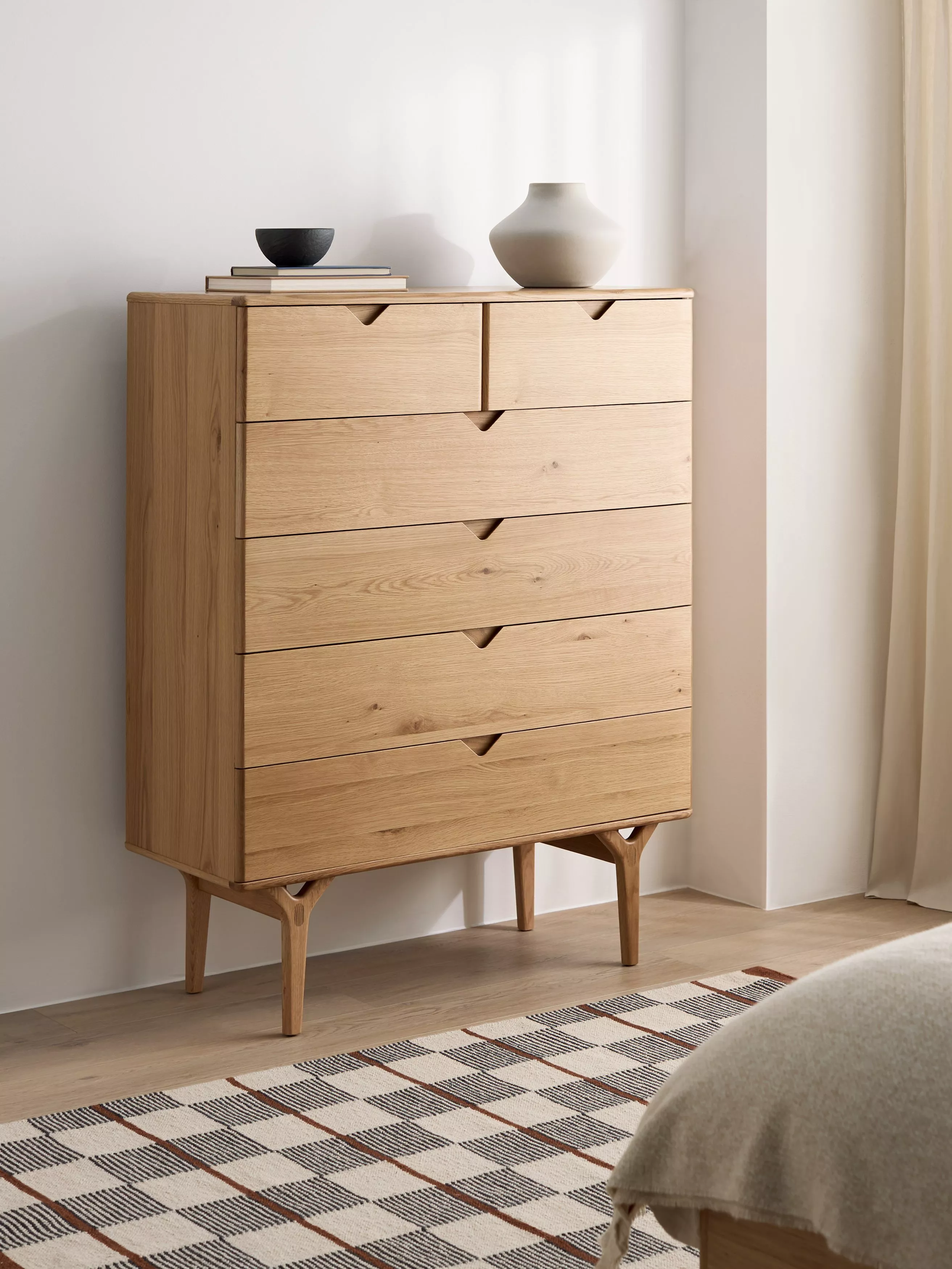 White wooden chest of drawers with round mirror, vase and books in a bright modern bedroom interior