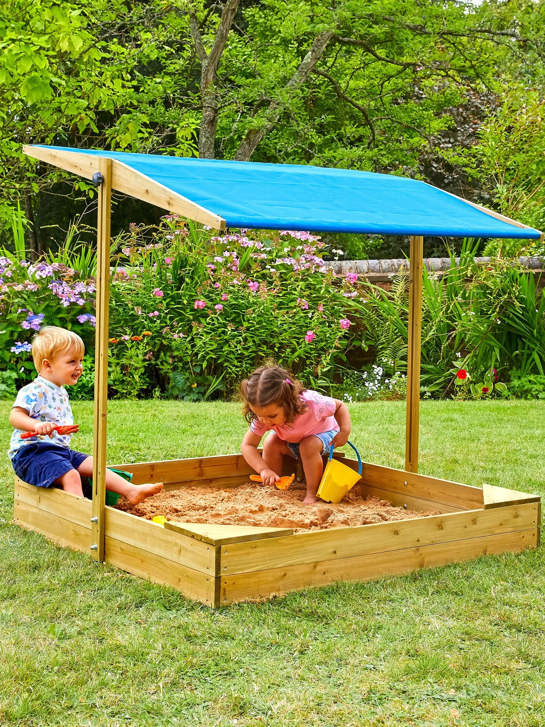 Two young children playing in a sandpit with buckets and spades