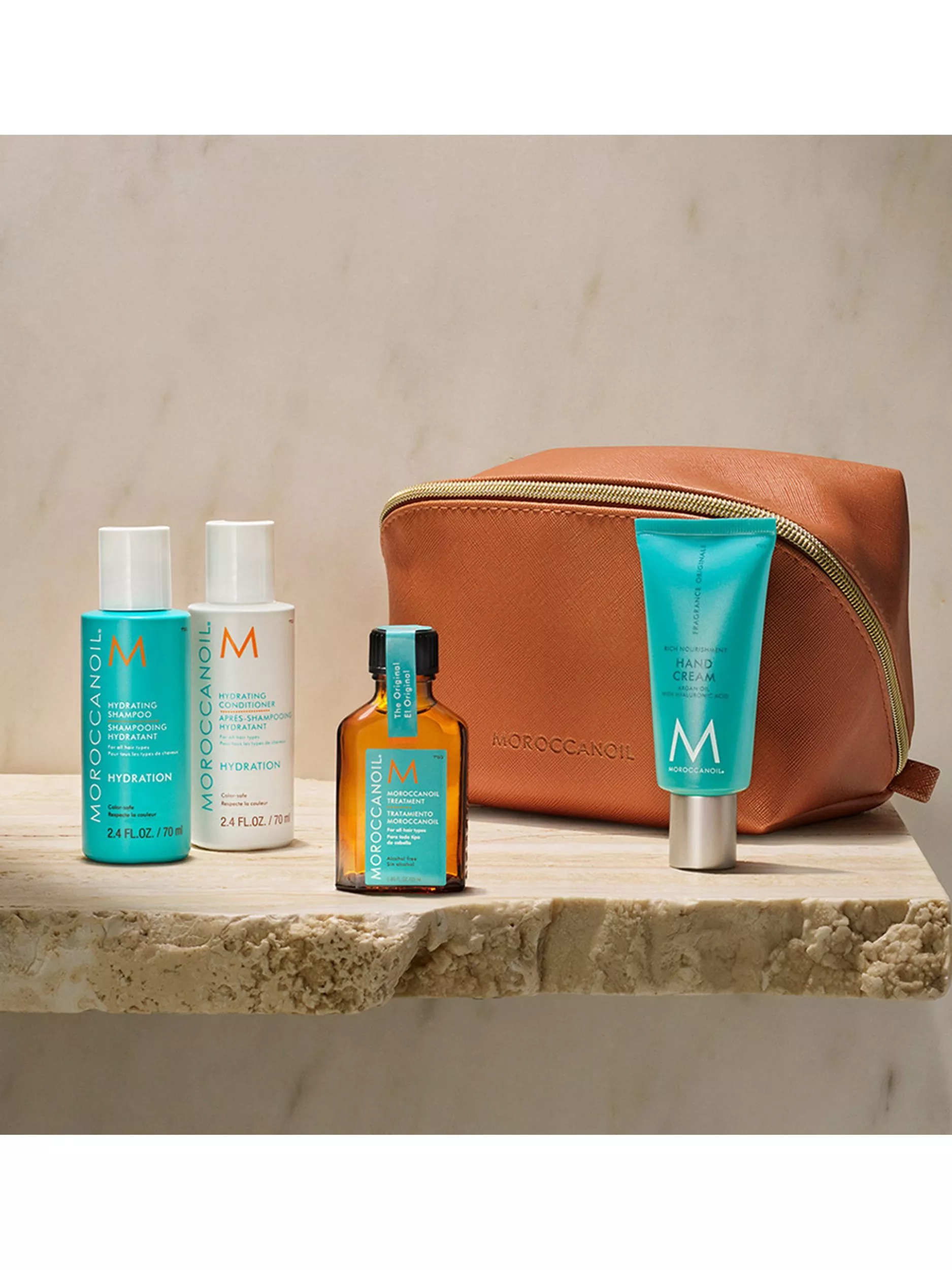 Moroccanoil products displayed on a marble surface with a leather pouch, featuring shampoo, conditioner, and hand cream.