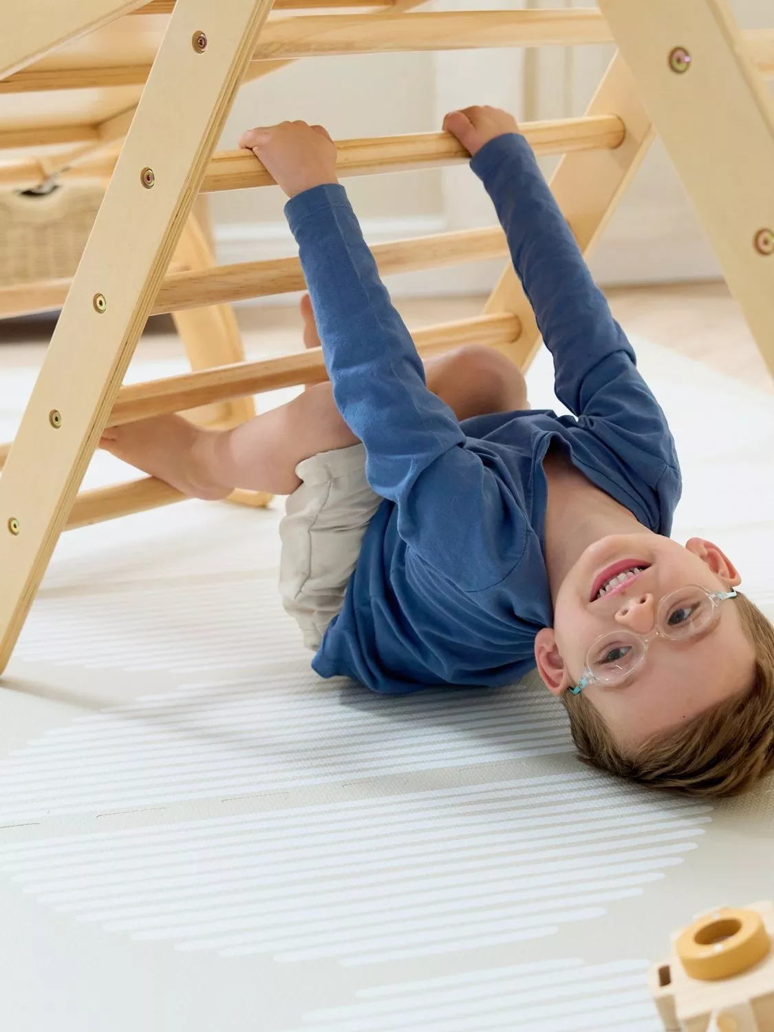 Young boy hanging upside down from a wooden climbing frame