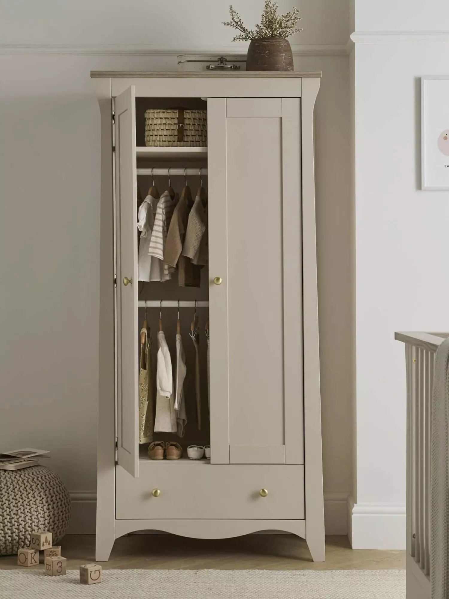 Cream wooden nursery wardrobe with open door, hanging baby clothes, shelf basket and drawer storage in bedroom