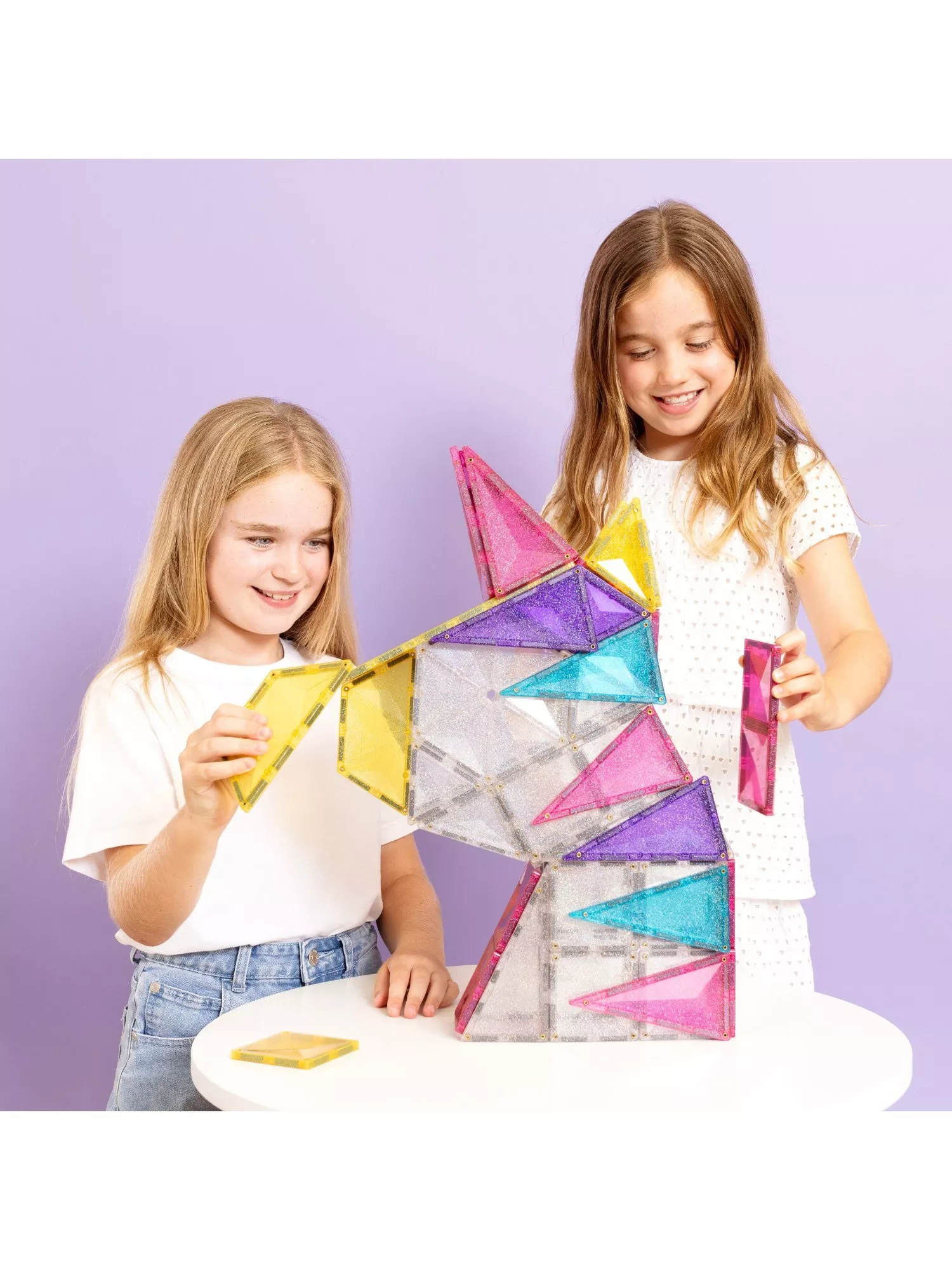 Two girls building a colourful magnetic tile unicorn model on a table, creative STEM construction toy play