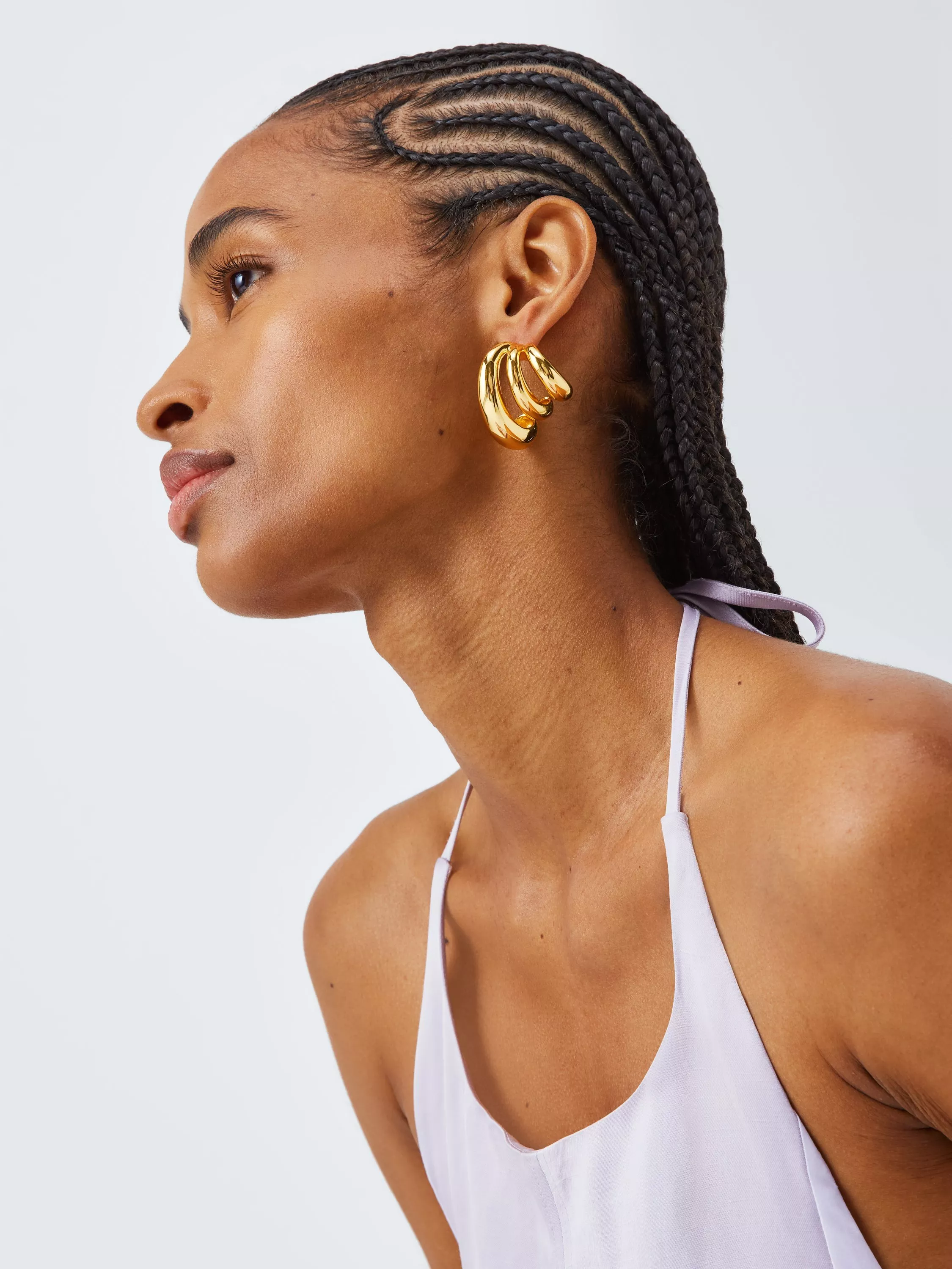 Side profile of woman with cornrow braids, wearing chunky gold hoop earrings and a lilac halterneck top.
