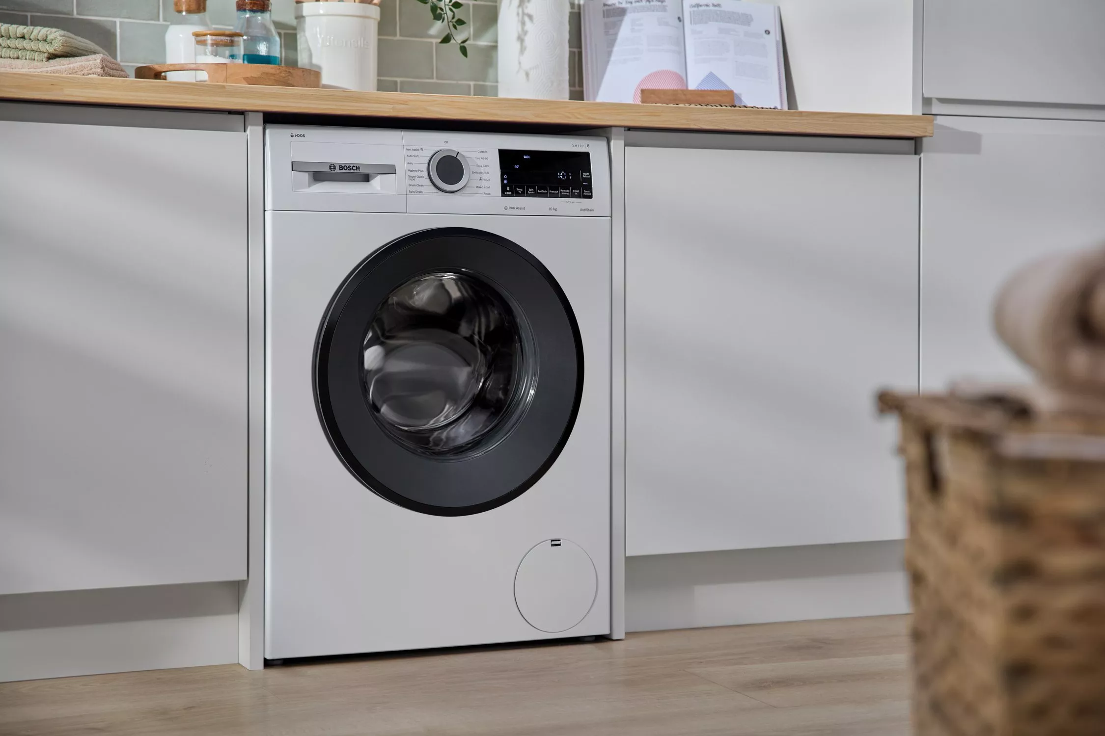 Integrated front-loading washing machine under kitchen worktop with grey cabinets, clean modern laundry space.