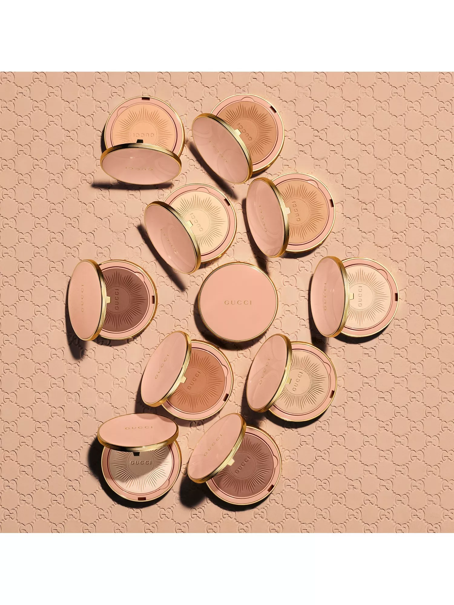Flat lay of Gucci bronzer and powder compacts in pink and gold on embossed beige background, luxury makeup packshot