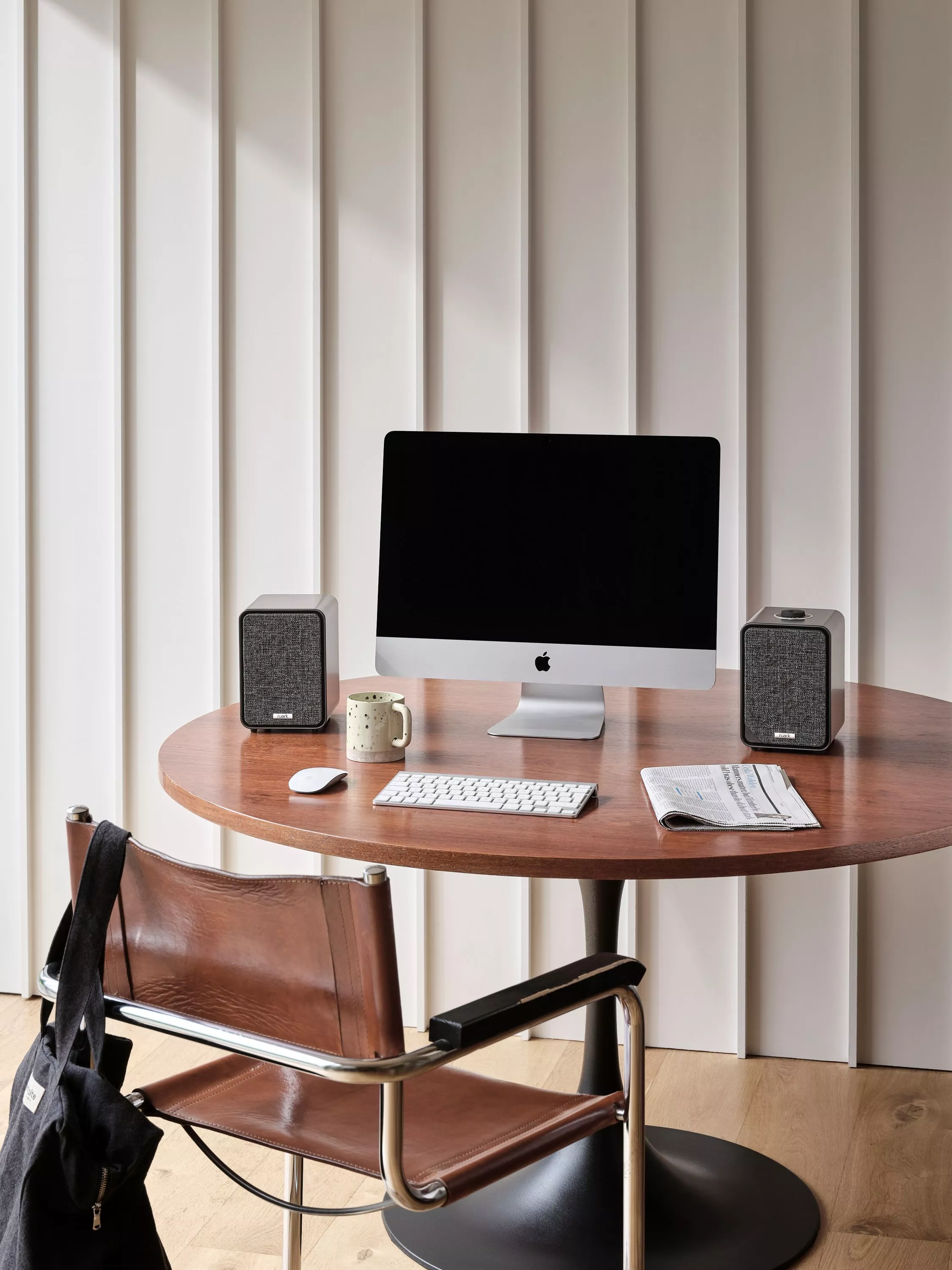 Modern home office desk with iMac, keyboard, mouse, coffee mug, speakers and newspaper on round table