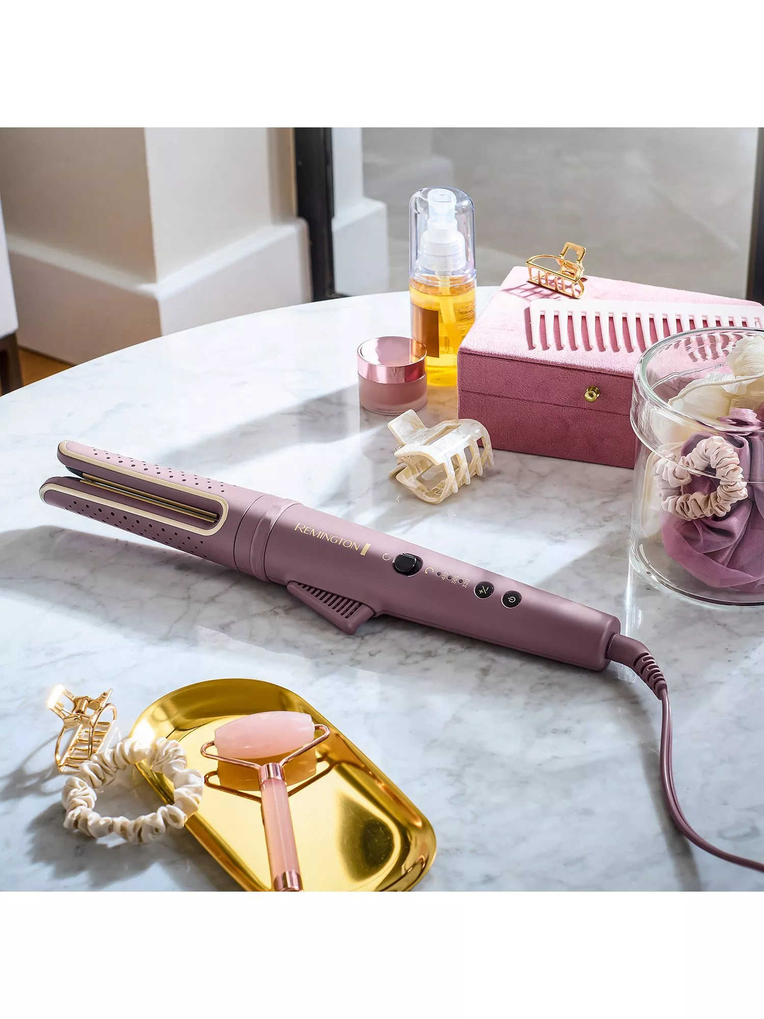 Pink Remington hair straightener on marble vanity with beauty accessories, clips, serum bottle and storage box