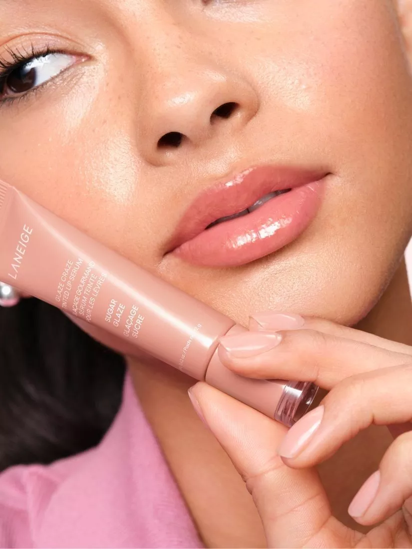 Close-up of a woman holding a pink Laneige lip product, showcasing her glossy lips and smooth complexion.
