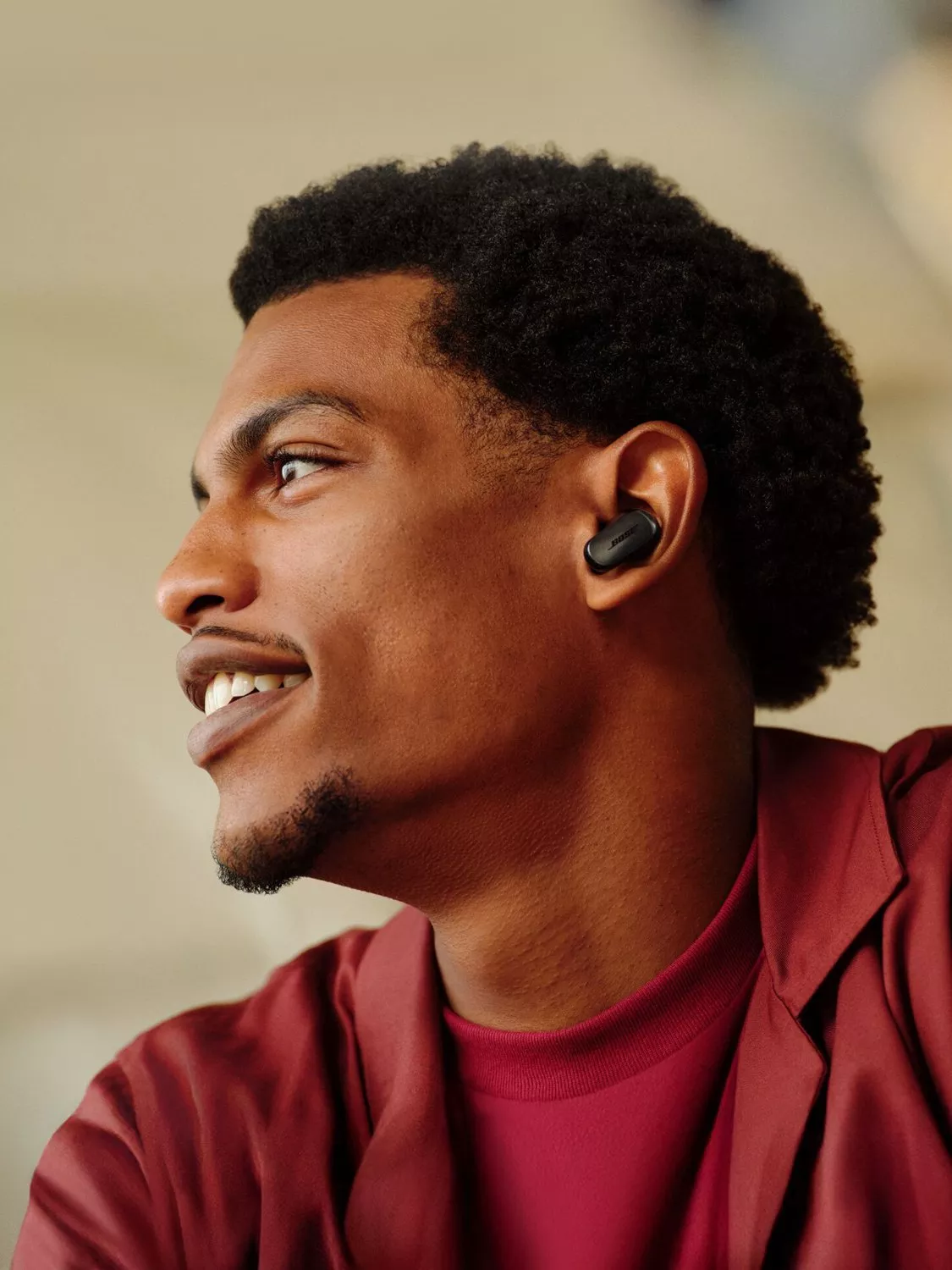Side profile of smiling man wearing black wireless earbuds, modern headphones for music and calls indoors