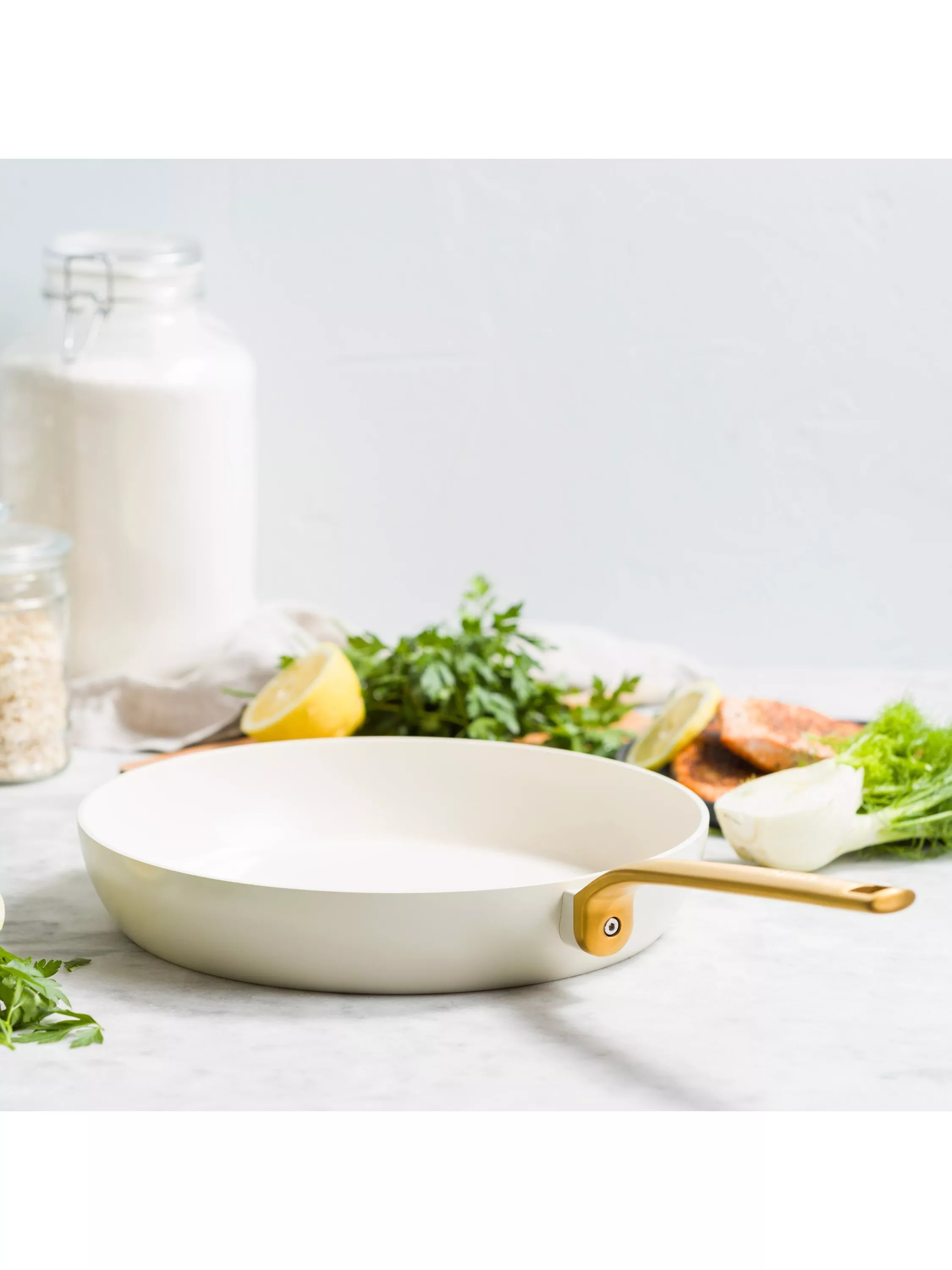 White ceramic frying pan on kitchen worktop with lemon, herbs, salmon and milk bottle in background