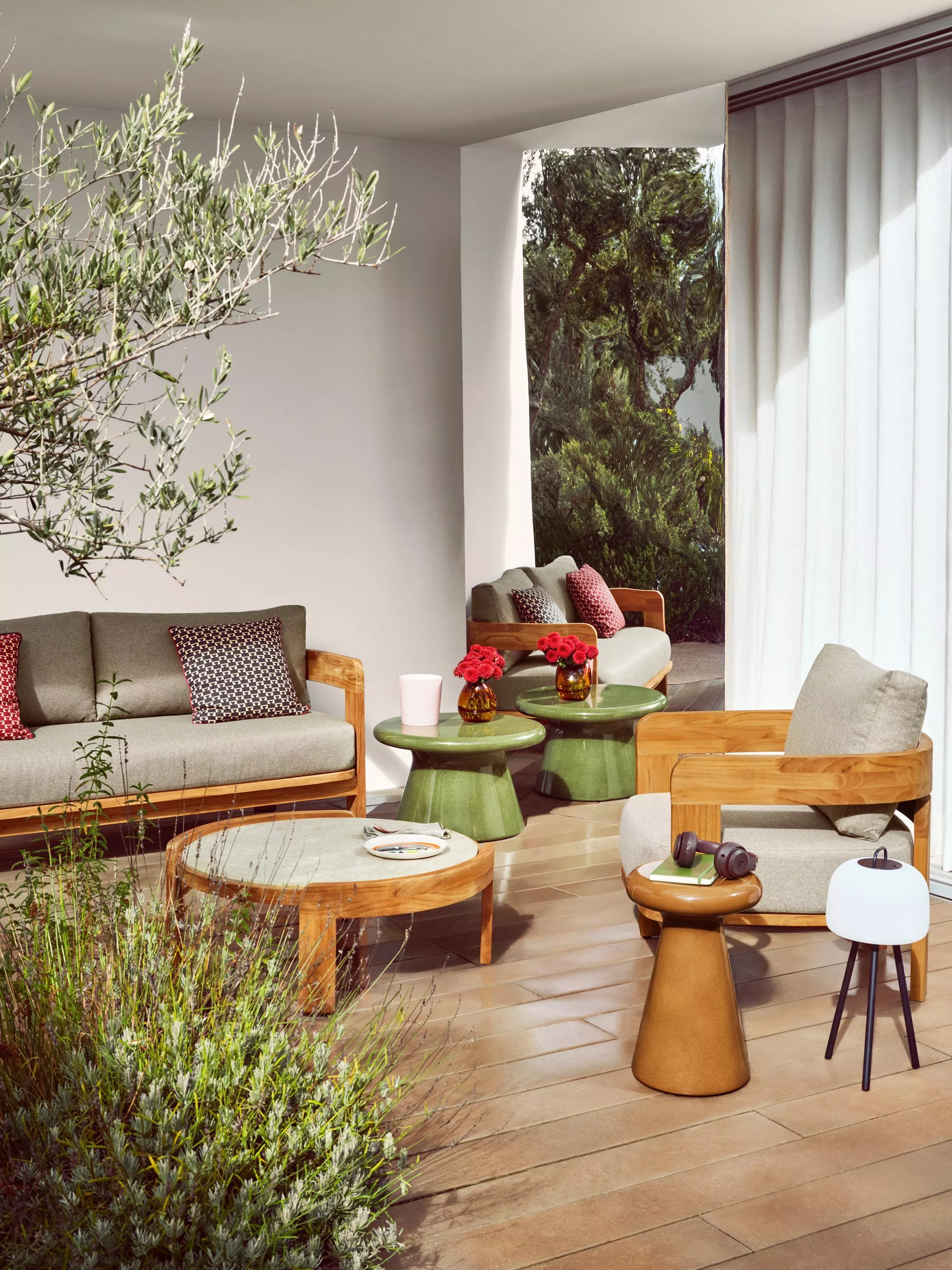 Sunlit modern patio lounge with wooden sofa and chairs, green side tables, coffee table and sheer curtains.