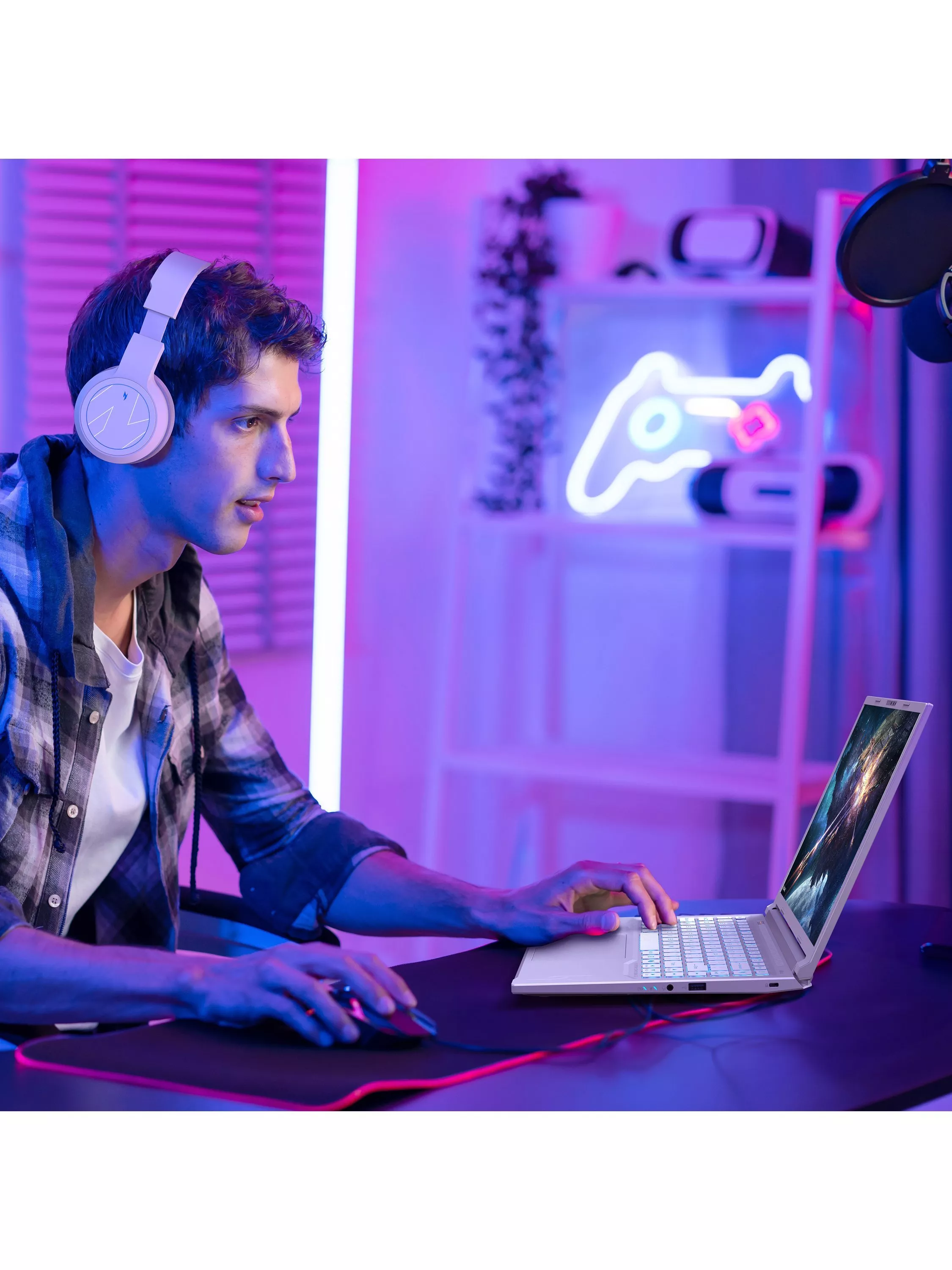PC gamer wearing headphones using a gaming laptop and mouse in a neon-lit streaming setup with microphone and LED sign