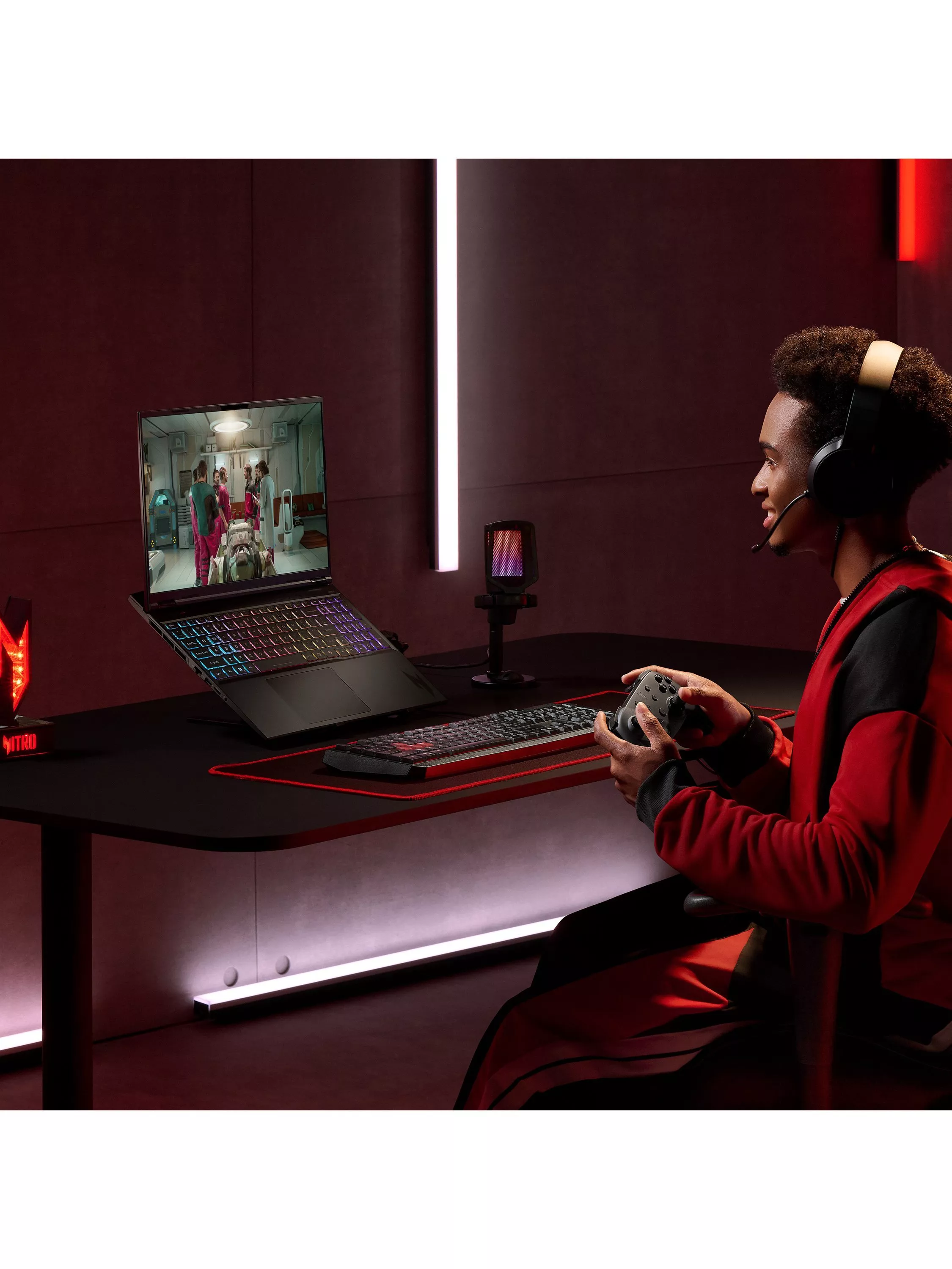Gamer wearing headset uses controller at RGB laptop gaming setup with microphone, streaming gameplay at desk