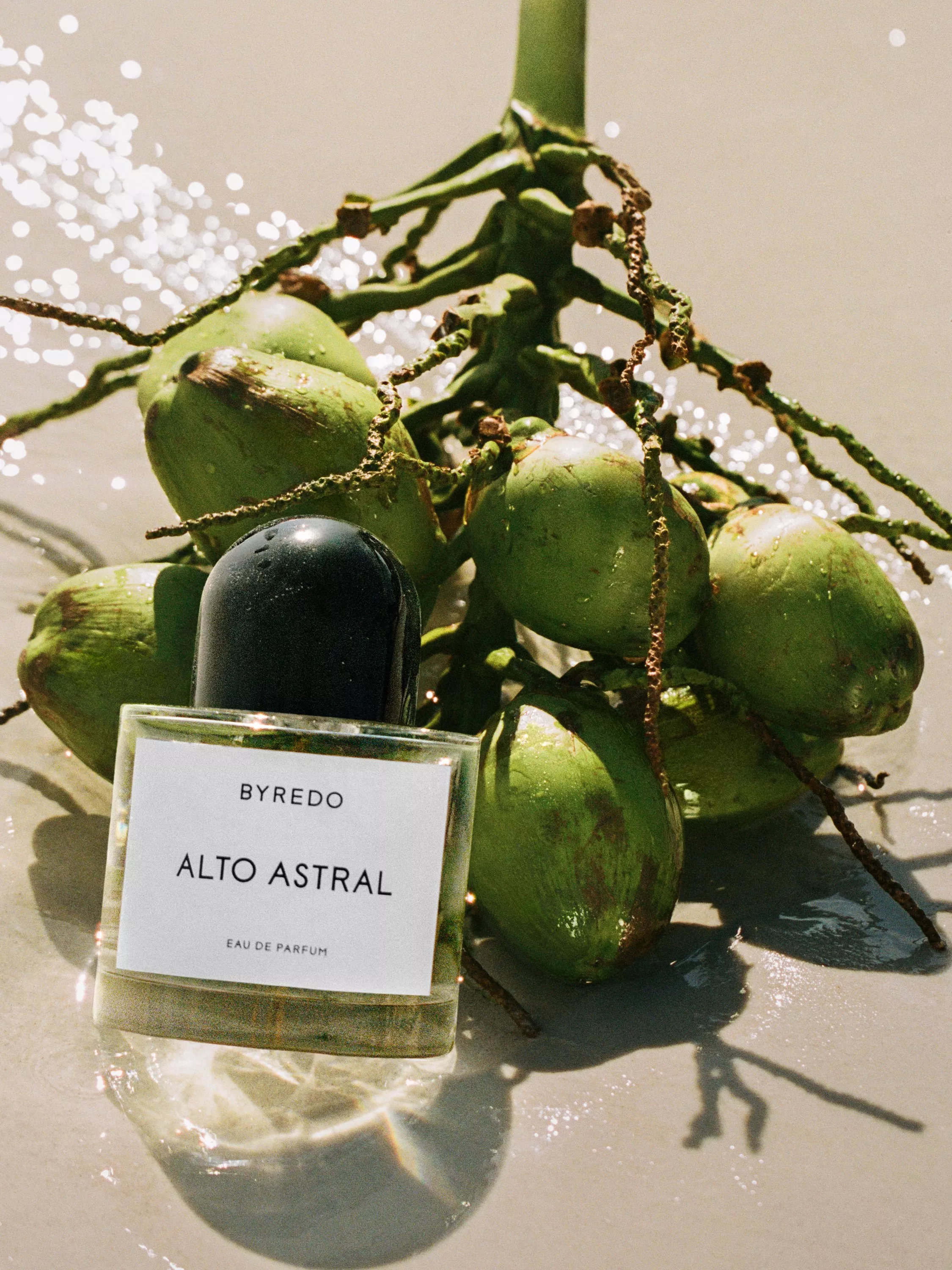 Byredo Alto Astral eau de parfum bottle beside fresh green coconuts in water, tropical fragrance scene.