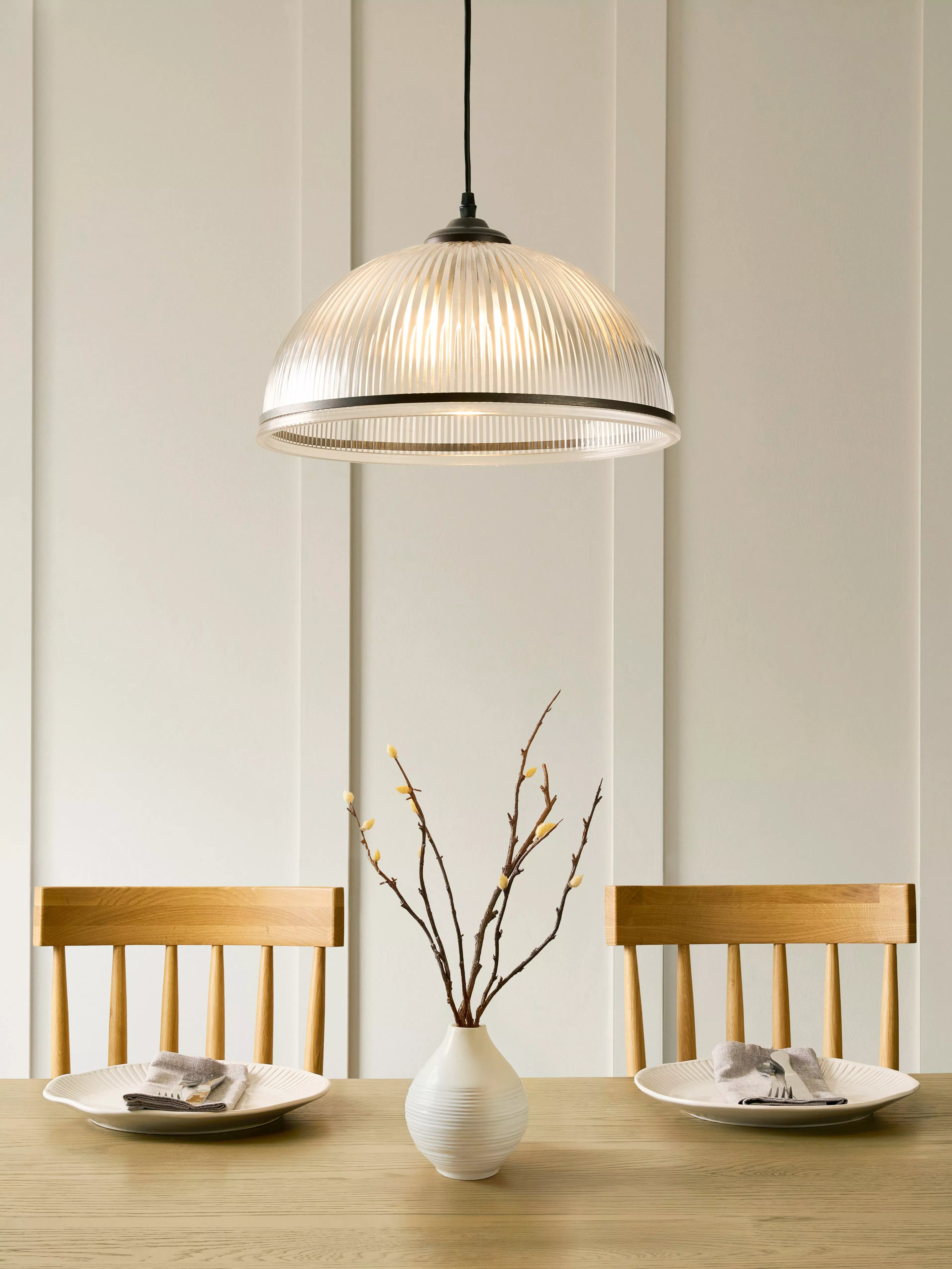 Modern dining setup with wooden chairs, a central vase with branches, and a stylish pendant light.