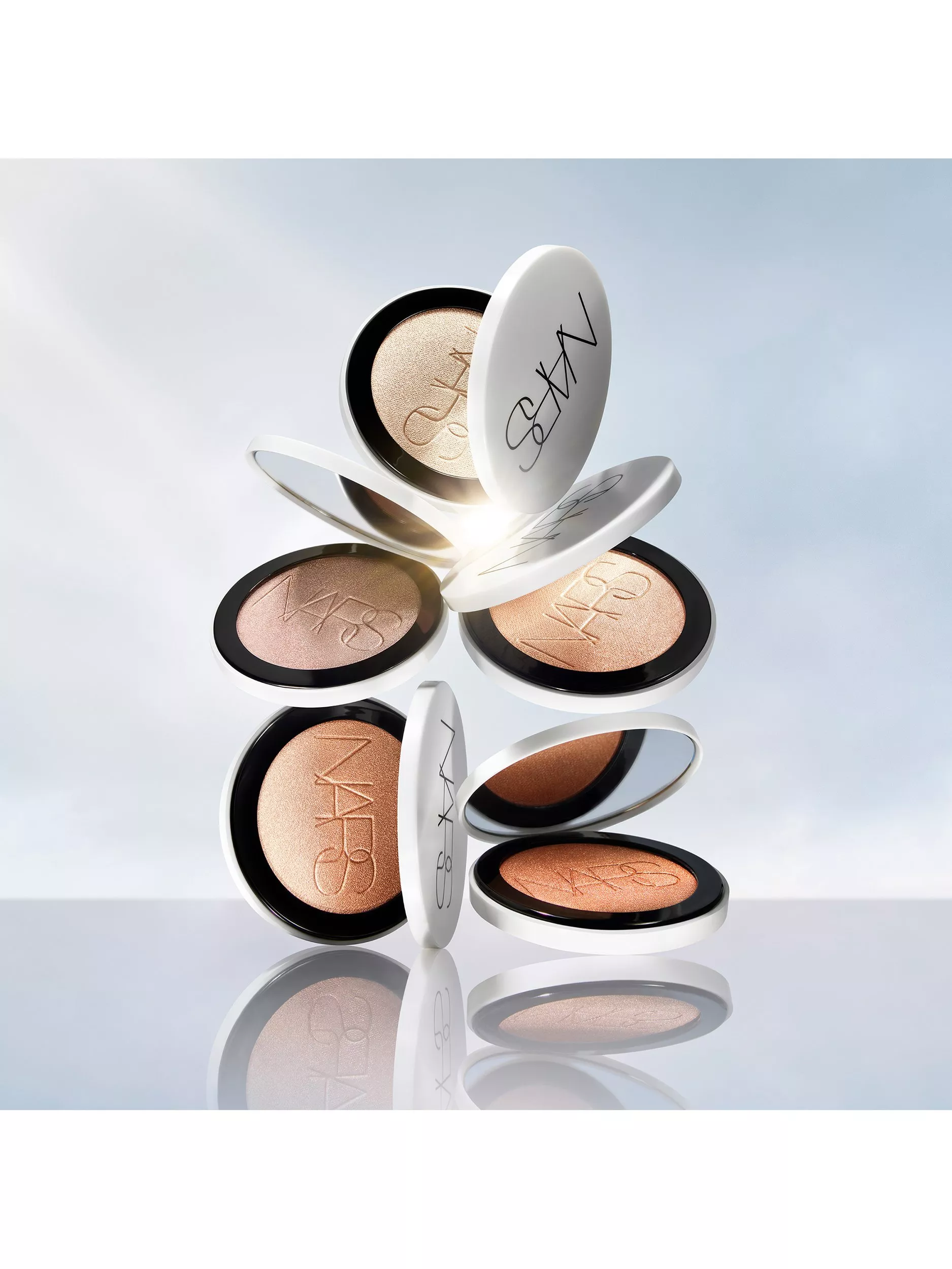 Floating NARS powder highlighter compacts in champagne and bronze shades with glowing shimmer on a reflective surface