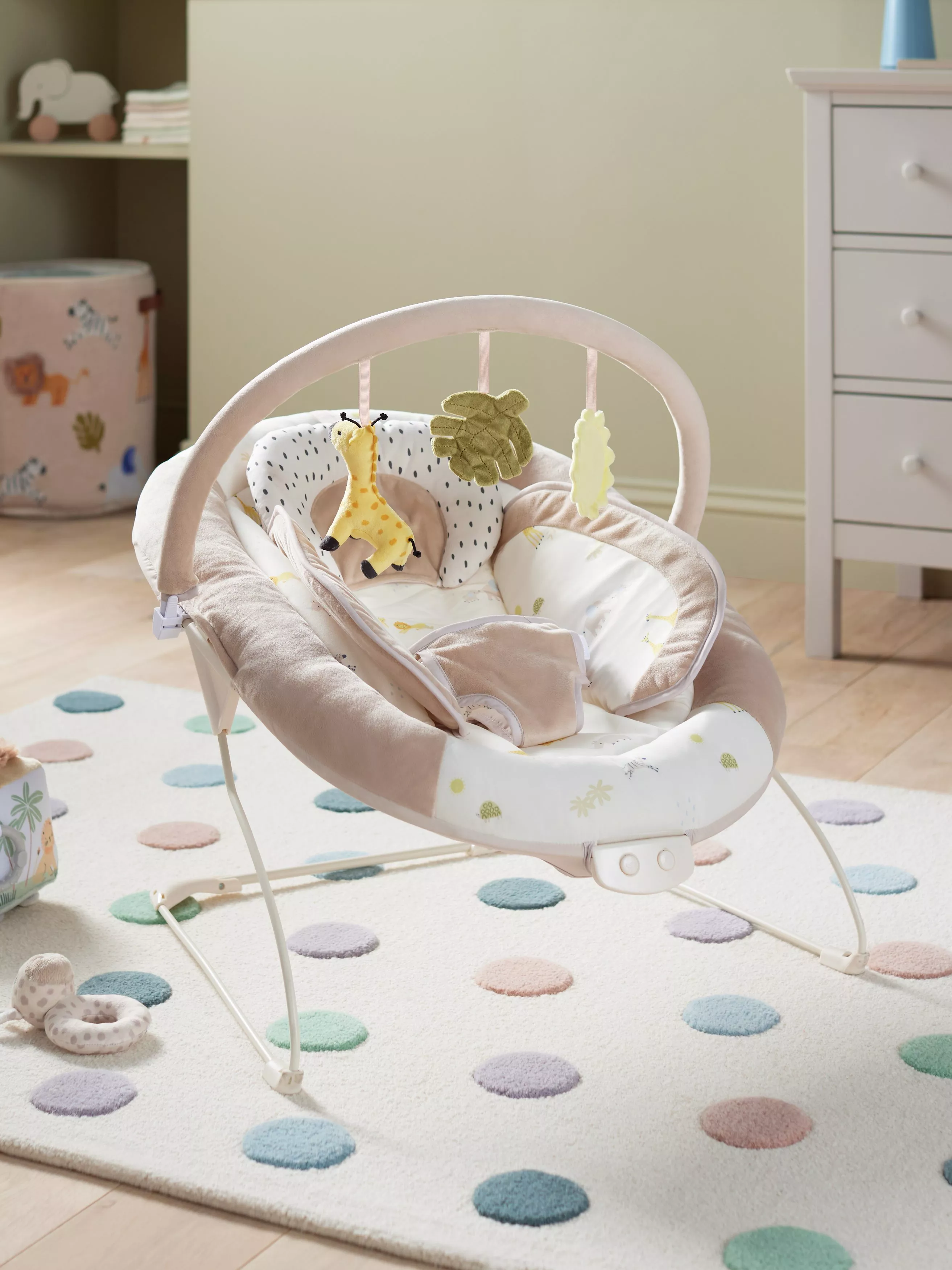 Safari-themed baby bouncer chair with hanging giraffe toy and leaf mobiles in a cosy nursery room setting