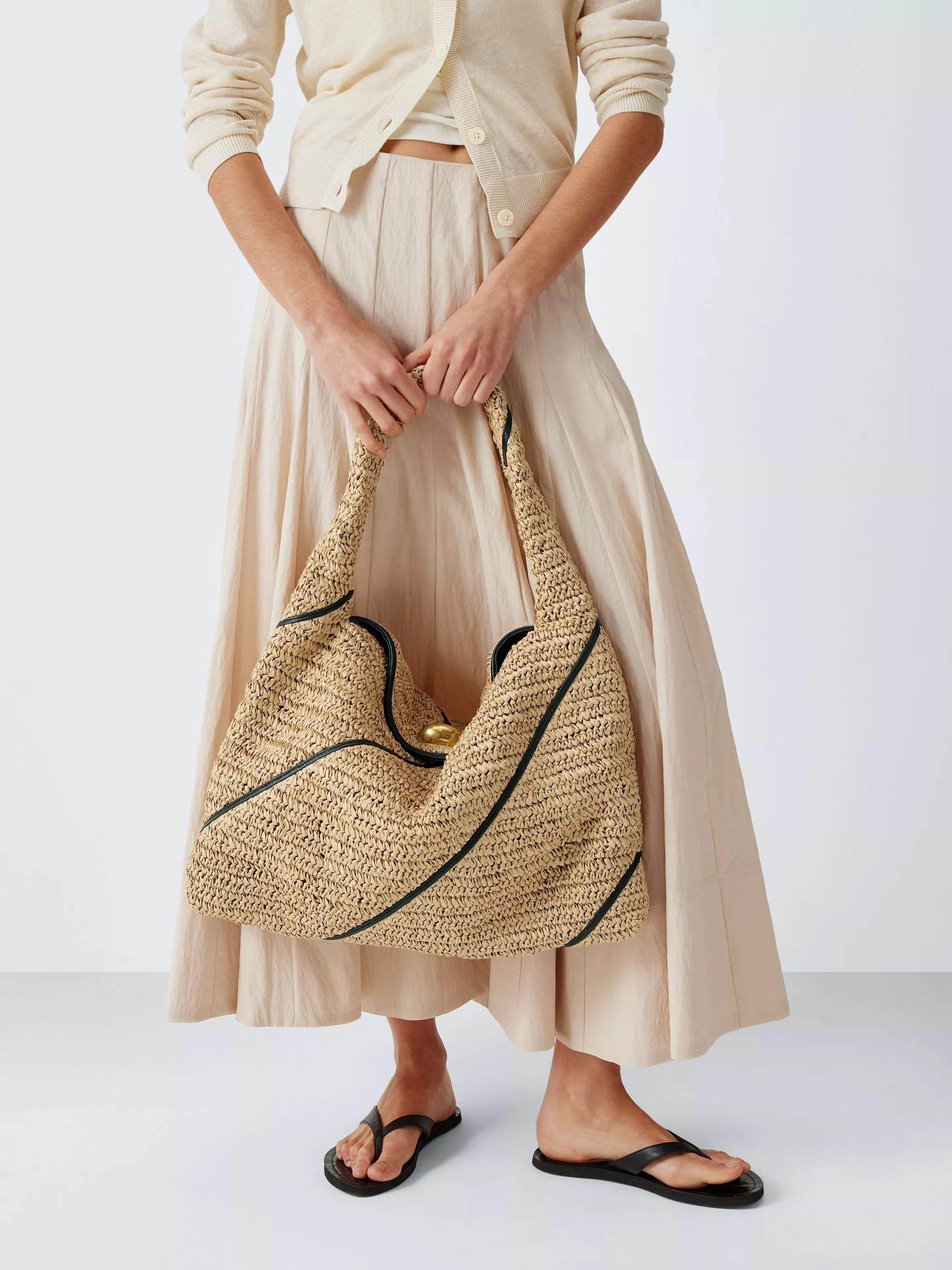 Woman in cream outfit carrying oversized woven straw tote bag with green trim