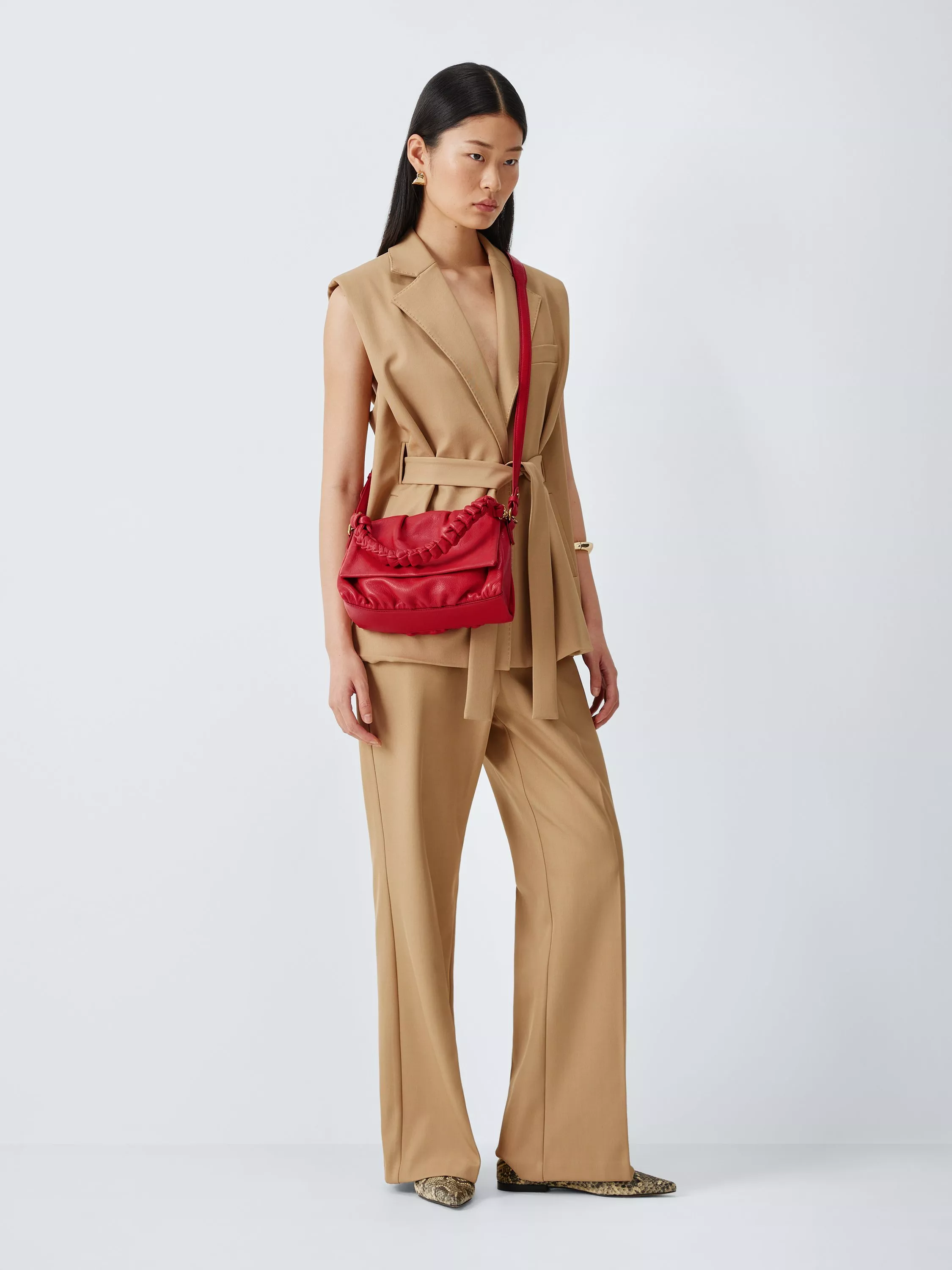 Elegant maroon handbag with gold accents, showcased outdoors on a mirrored surface by the seaside cliffs.