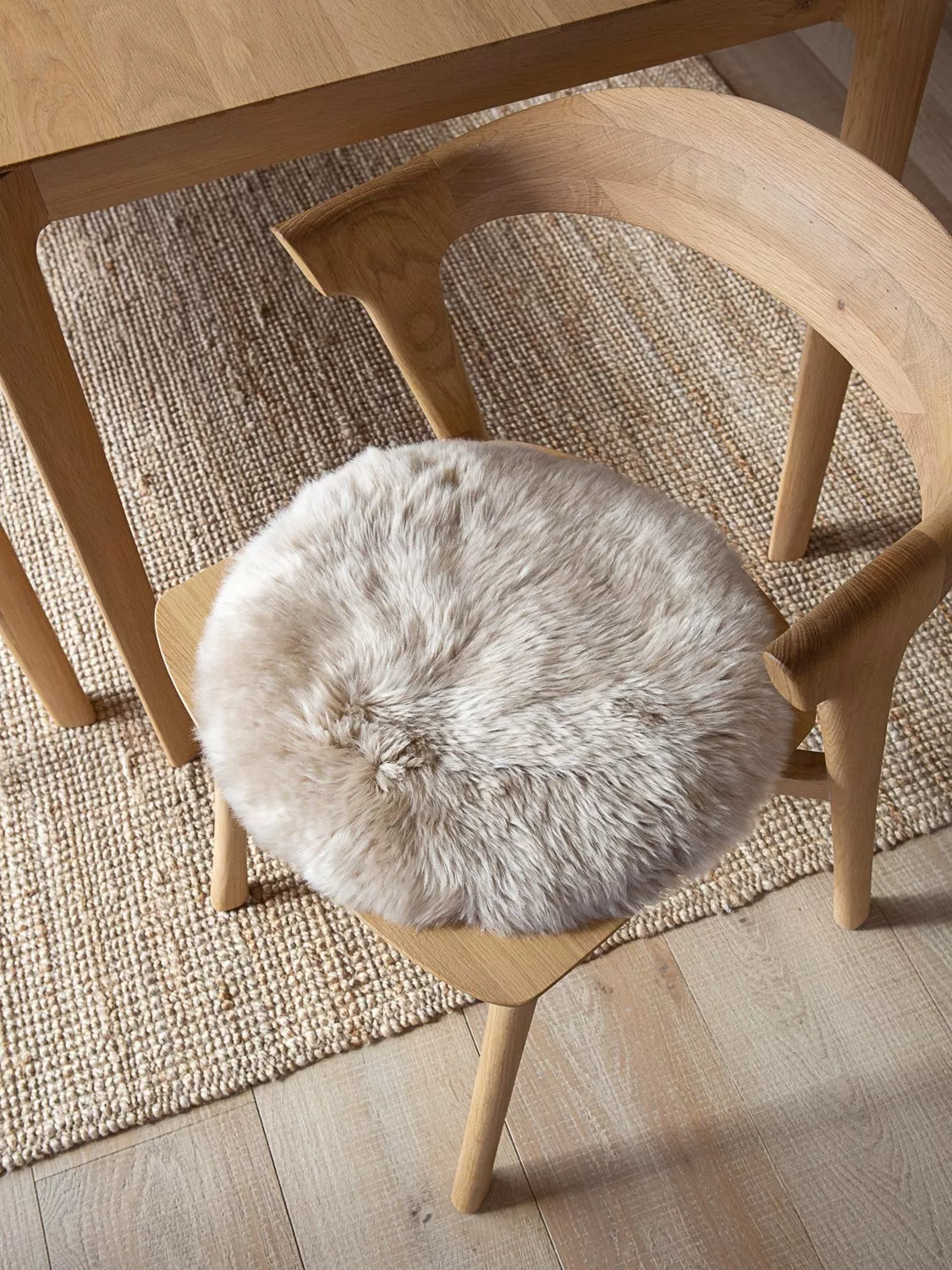 Oak dining chair with soft grey sheepskin seat pad beside wooden table on woven natural jute rug