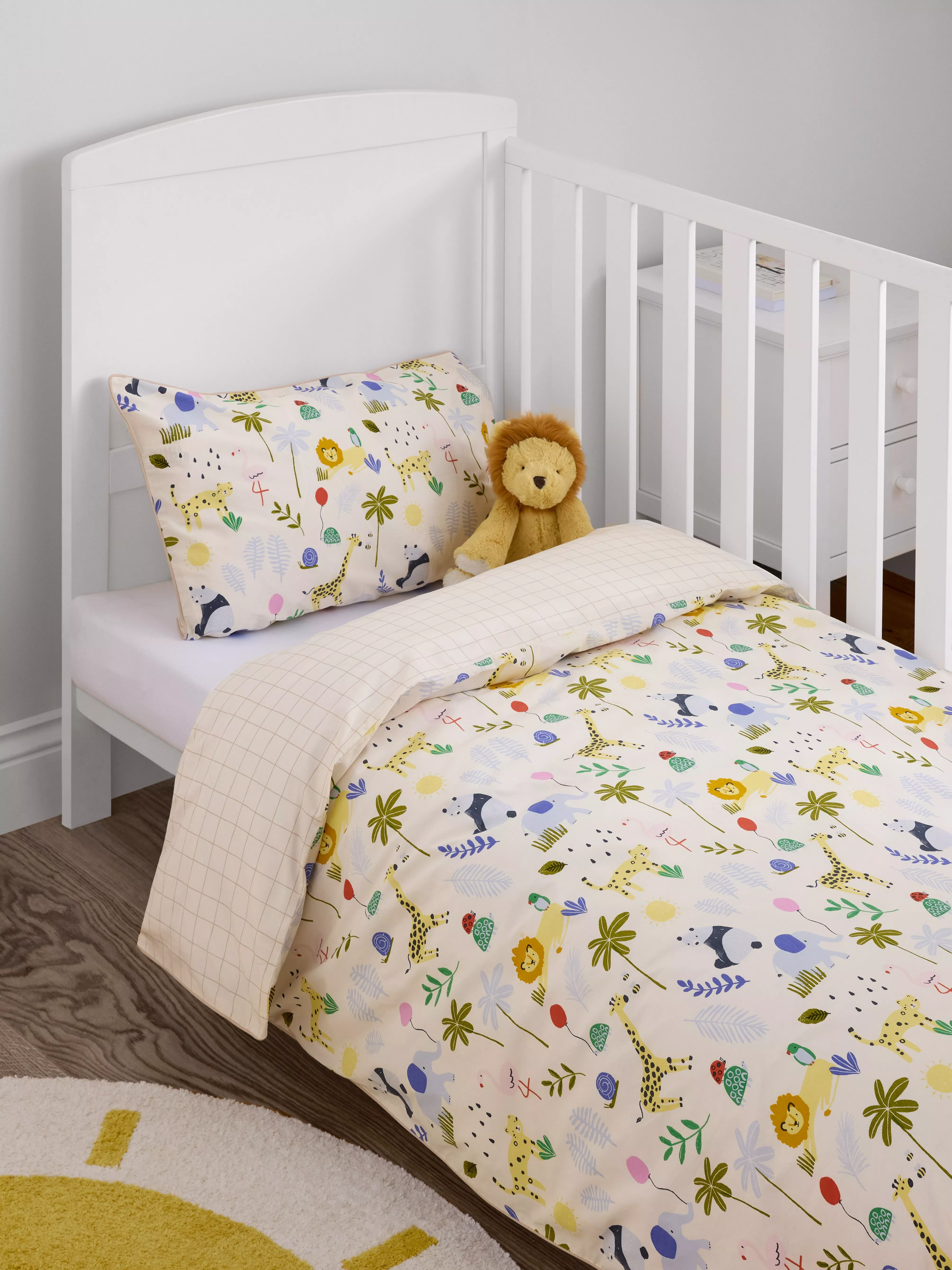 White toddler cot bed with safari animal duvet cover and pillowcase, plus plush lion toy in nursery room