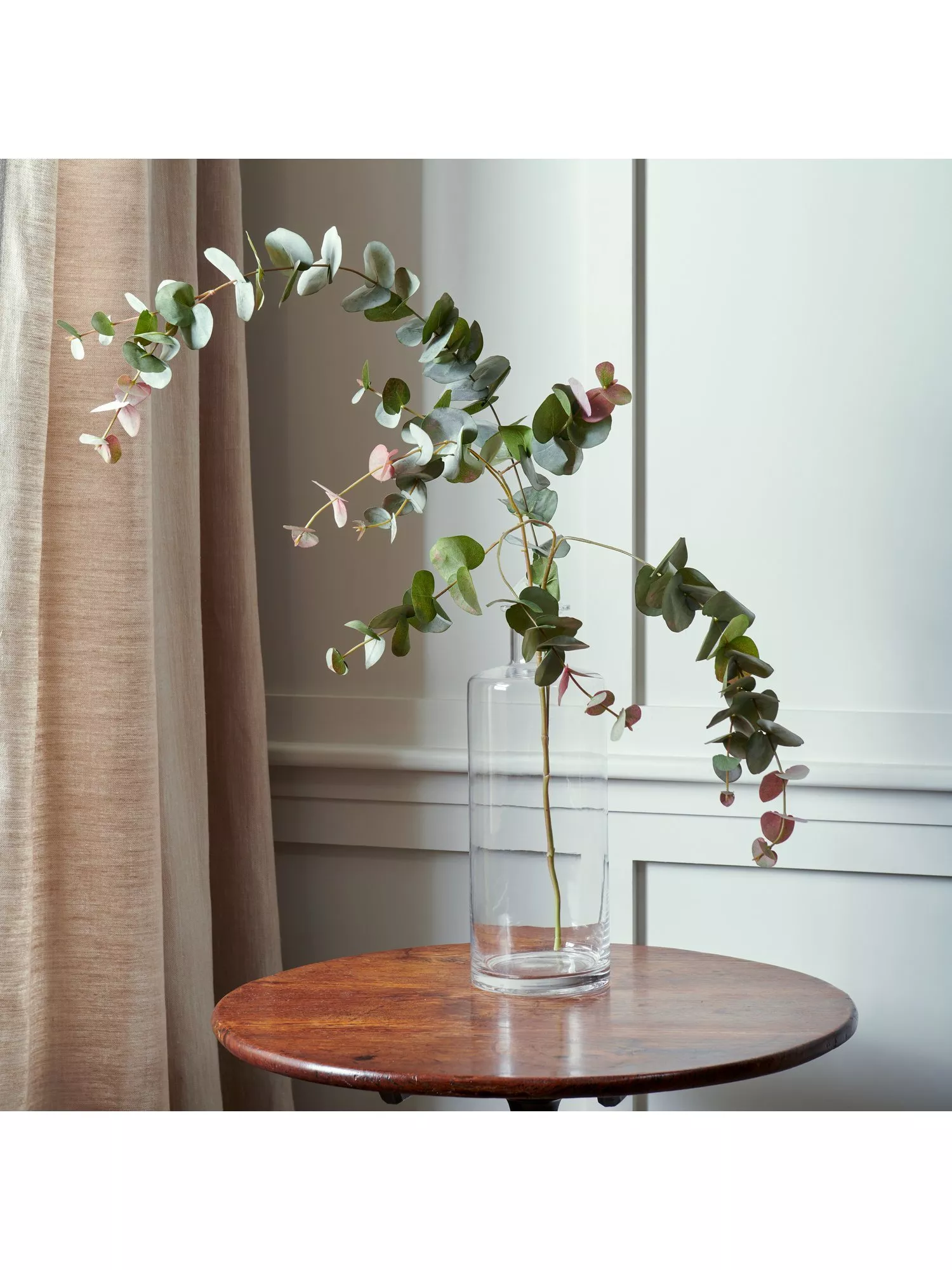 Artificial eucalyptus red box spray in a glass vase on a dark wood side table