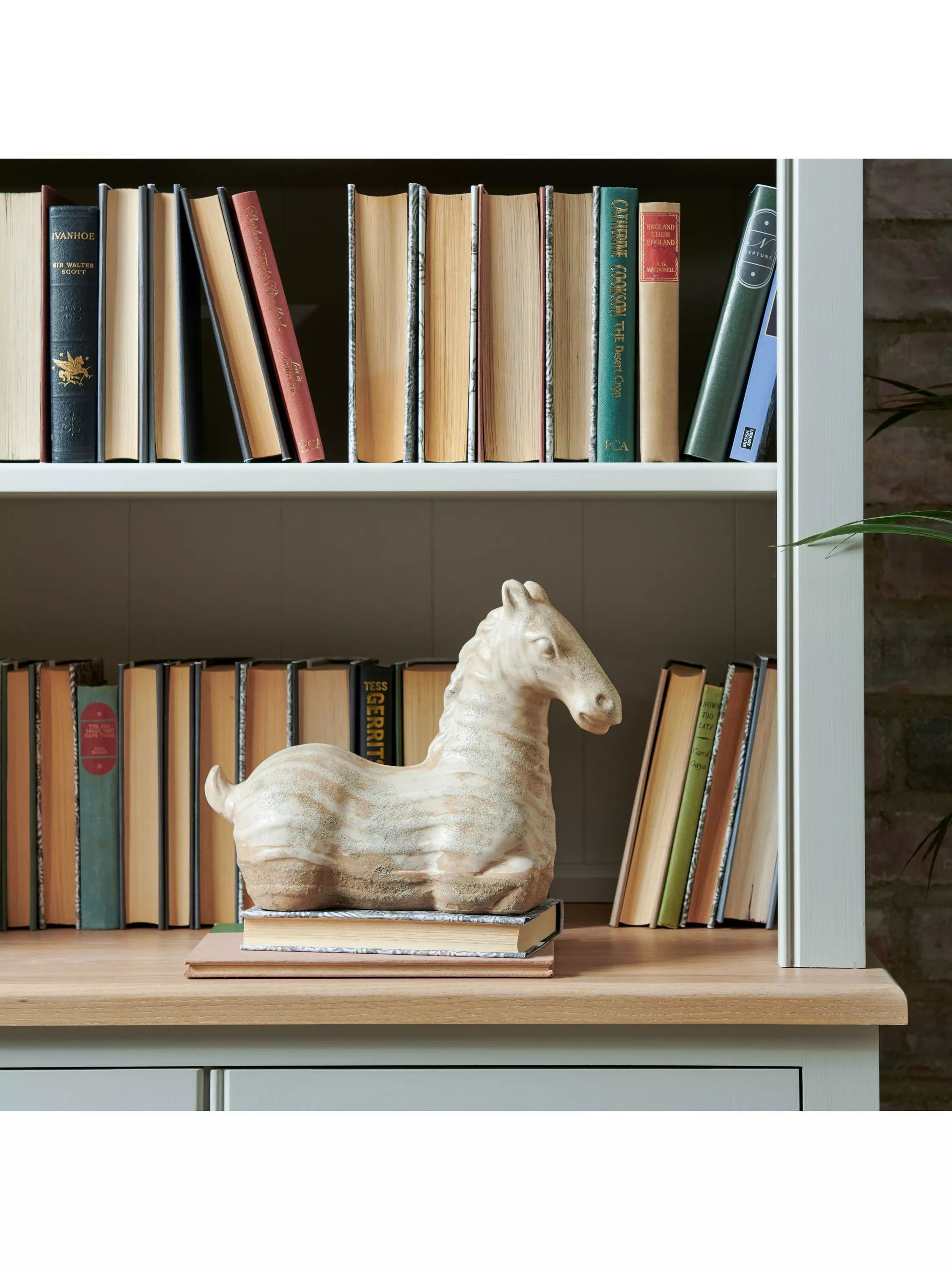 White bookcase with vintage hardbacks and a carved wooden horse ornament on shelf in cosy home library