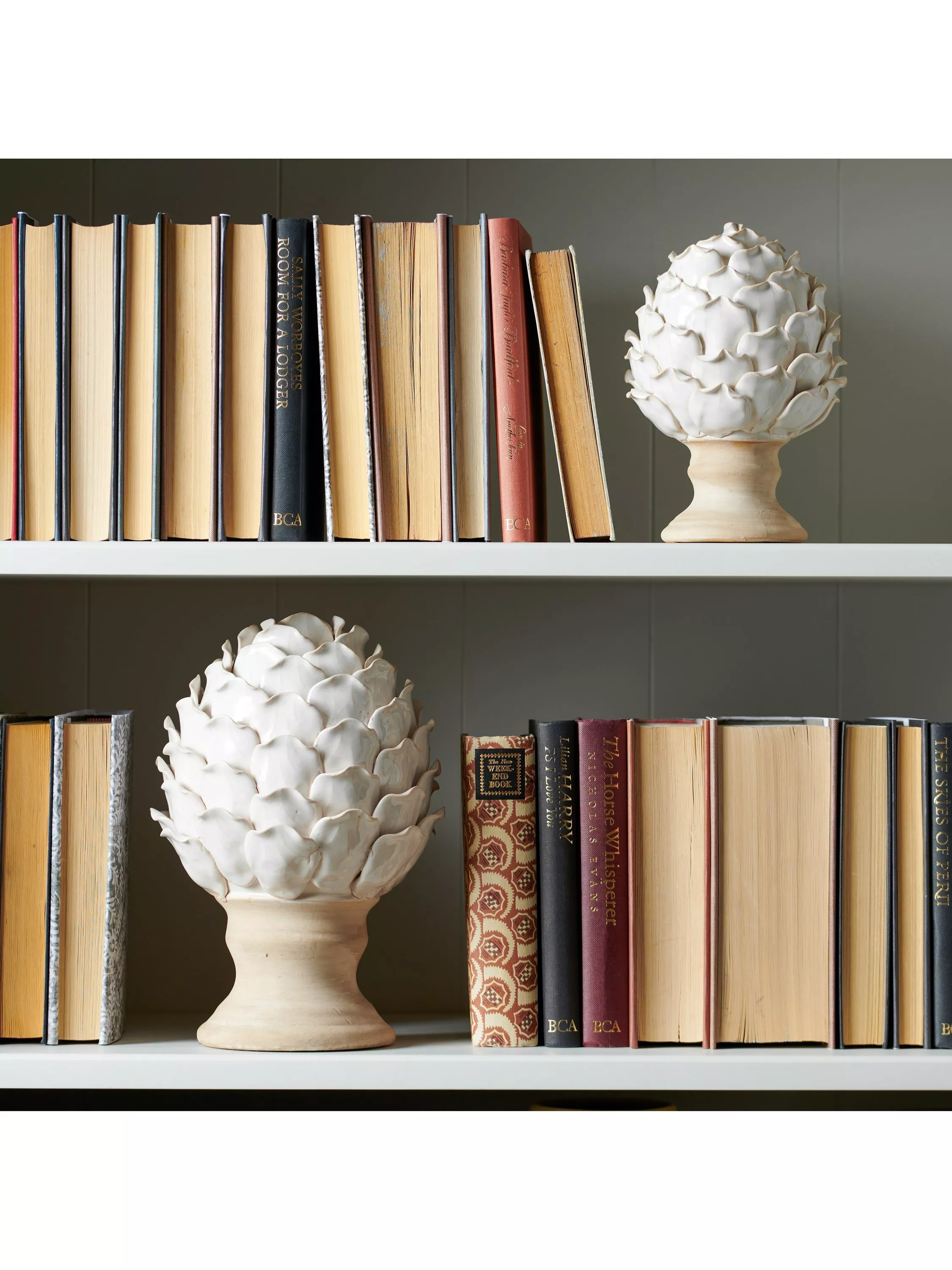 Modern bookshelf styling with vintage books and white ceramic artichoke ornaments on wooden bases