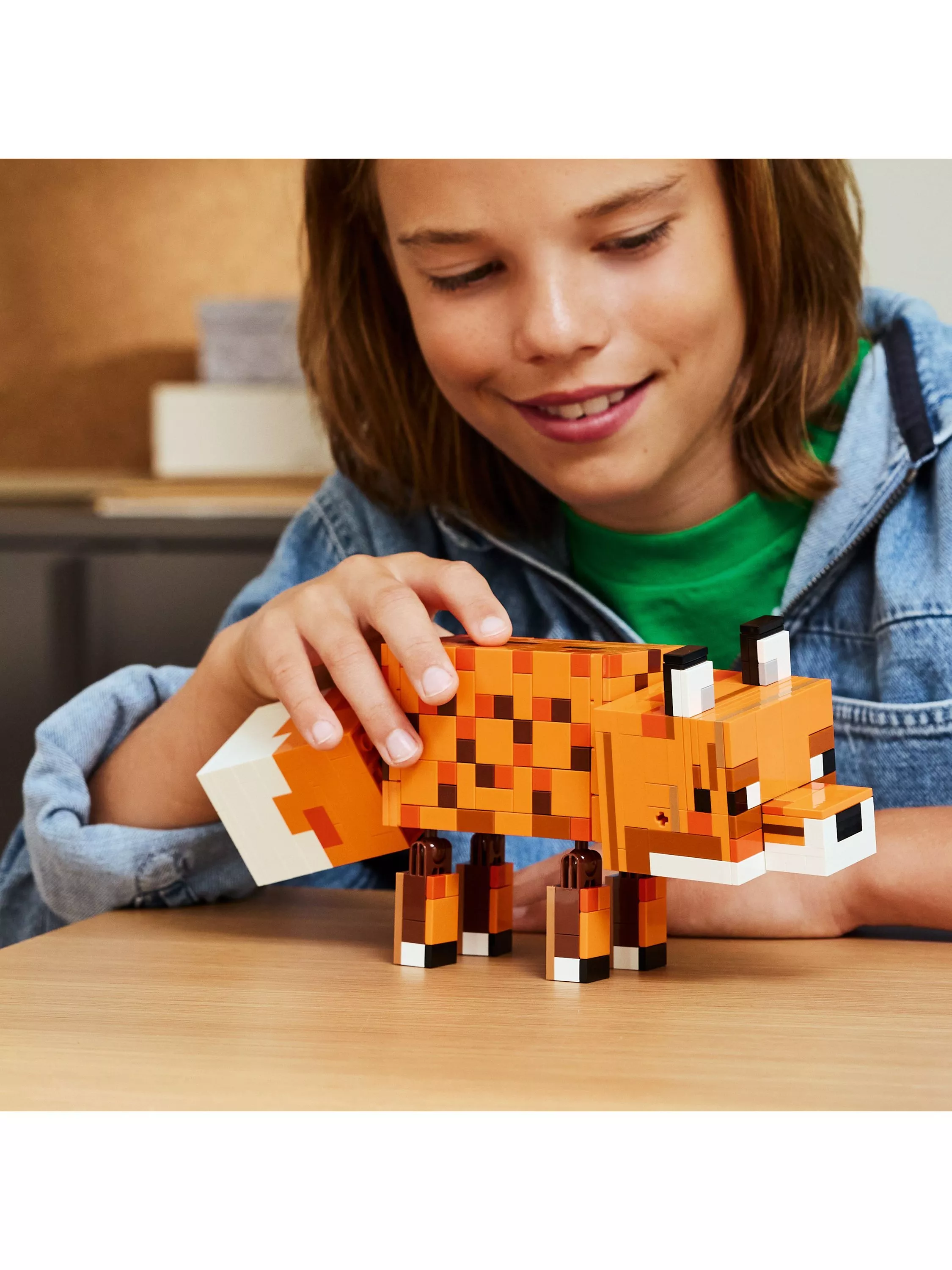 Child building a pixel-style LEGO fox model on a table, hands adjusting blocks in a close-up shot