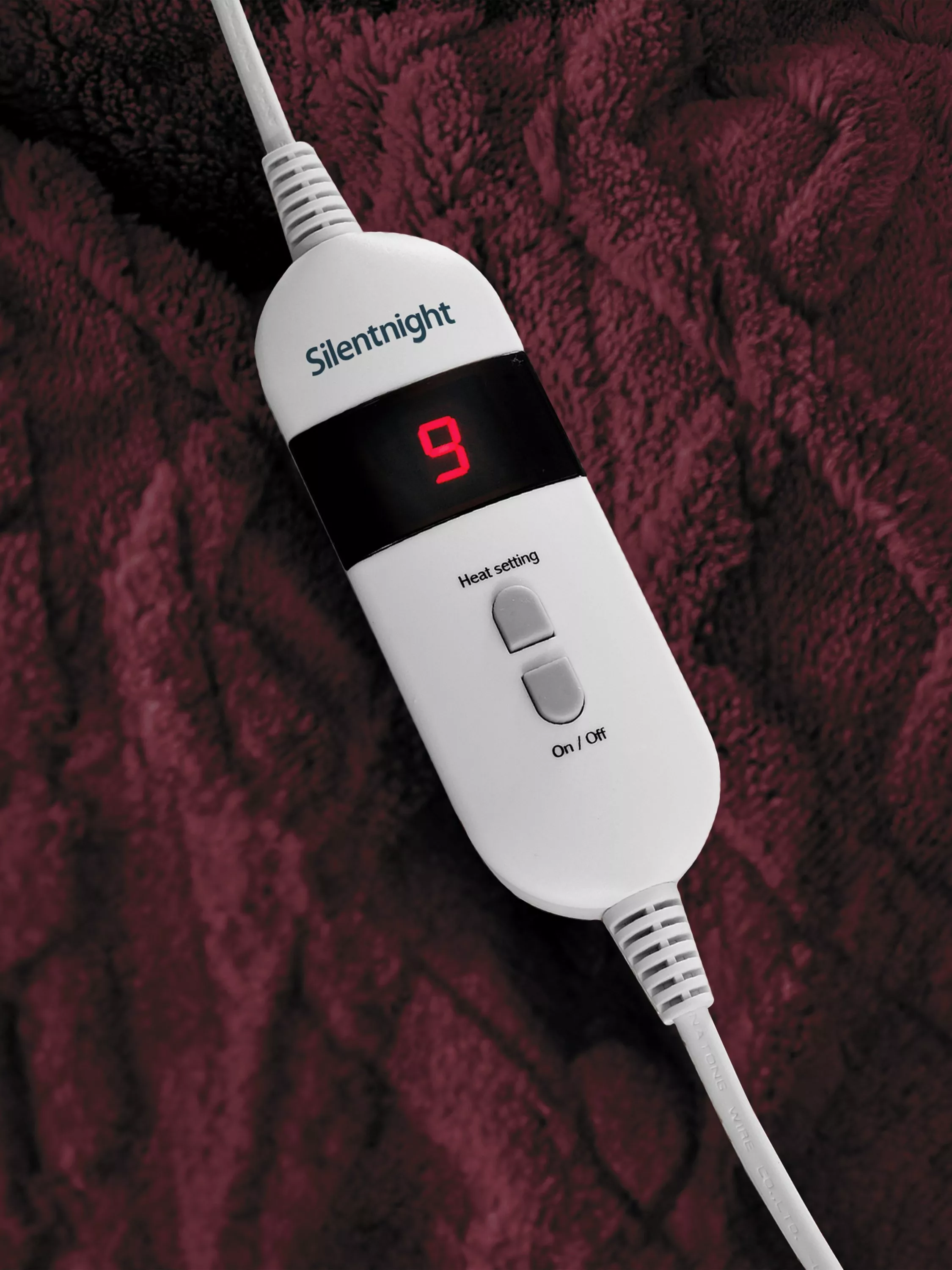 Silentnight electric heated blanket controller showing heat setting 9 on soft burgundy fleece fabric background