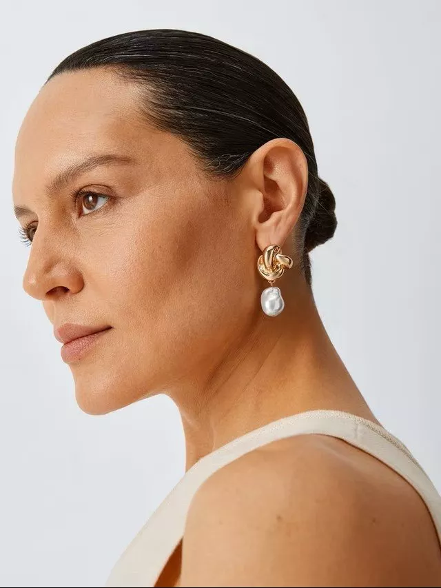 Elegant gold and pearl drop earring on a person with dark hair styled in a sleek bun.