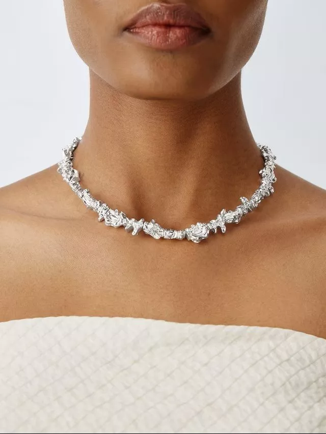 A woman wearing a textured silver necklace on a bare neck, complemented by a white textured top.