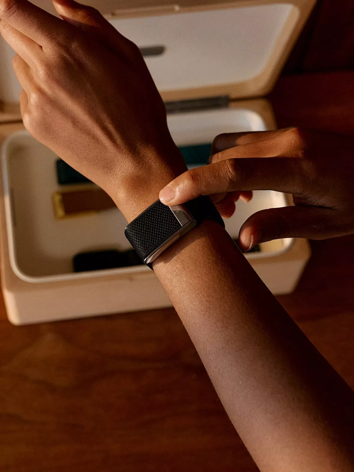 Close-up of person tapping a black fitness tracker on wrist, health monitoring wearable in warm indoor light